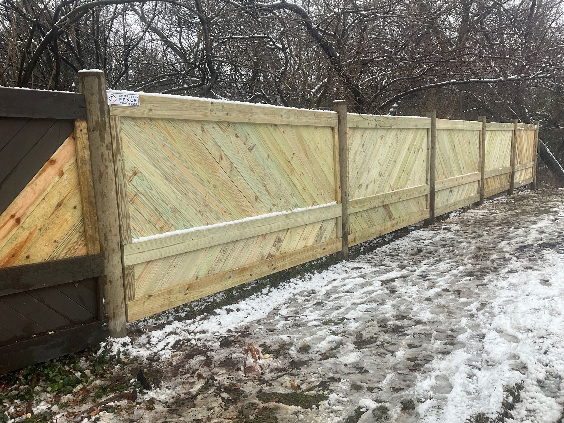 Wooden fence with diagonal planks, in a snowy outdoor setting.