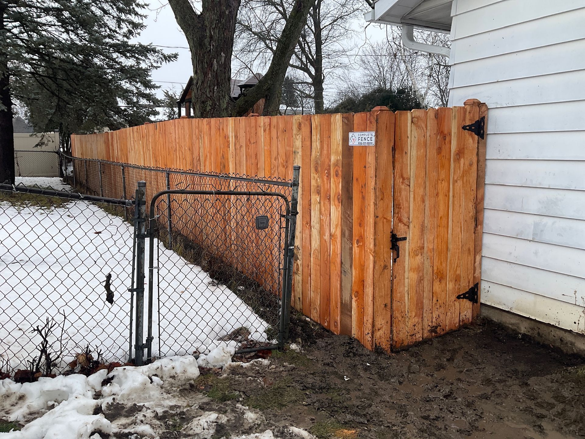 Wooden fence with gate, bordering a house with chain link fencing. Winter scene with snow.