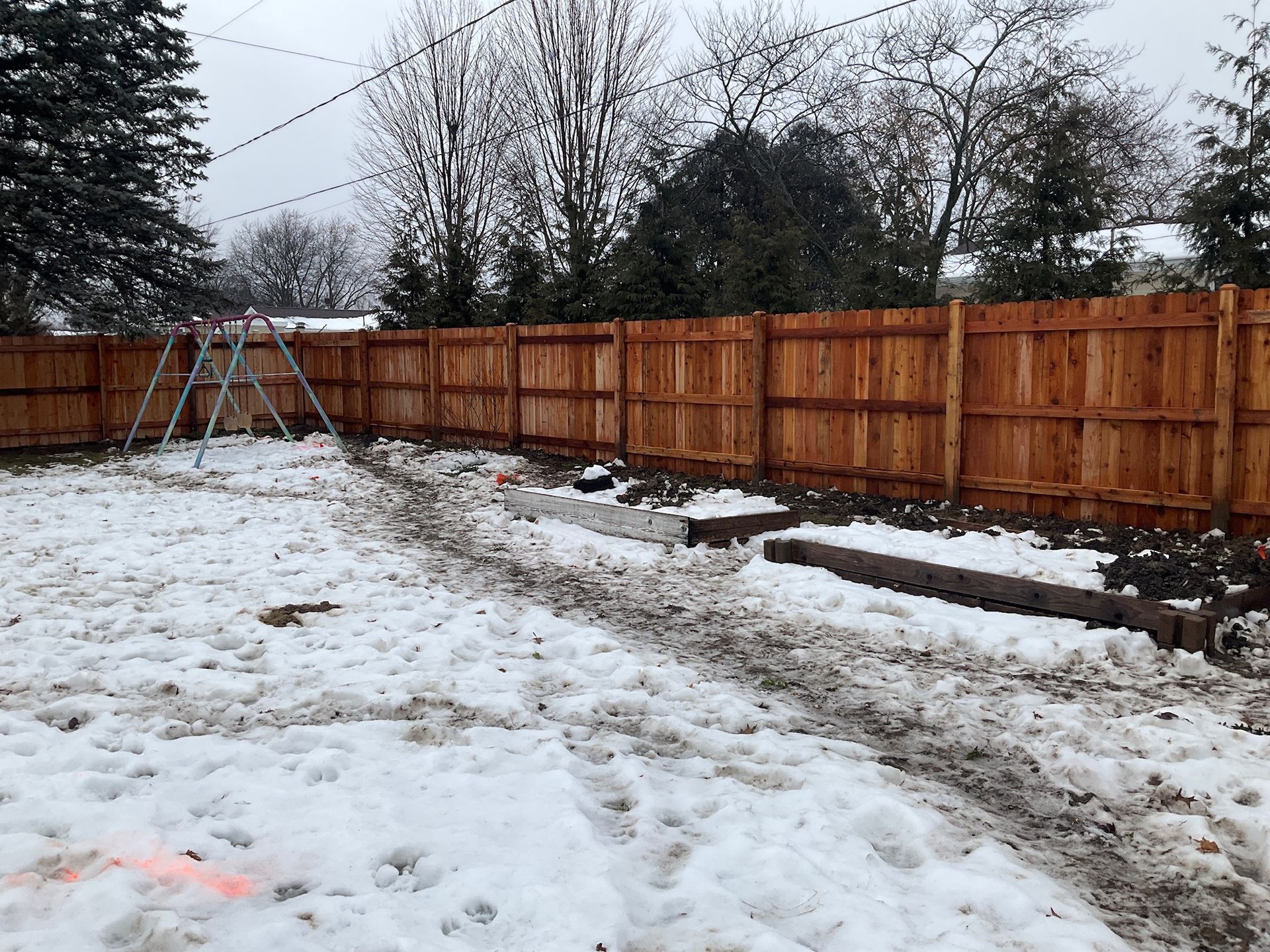 Snowy backyard with a wooden fence, pathway, and ladder.