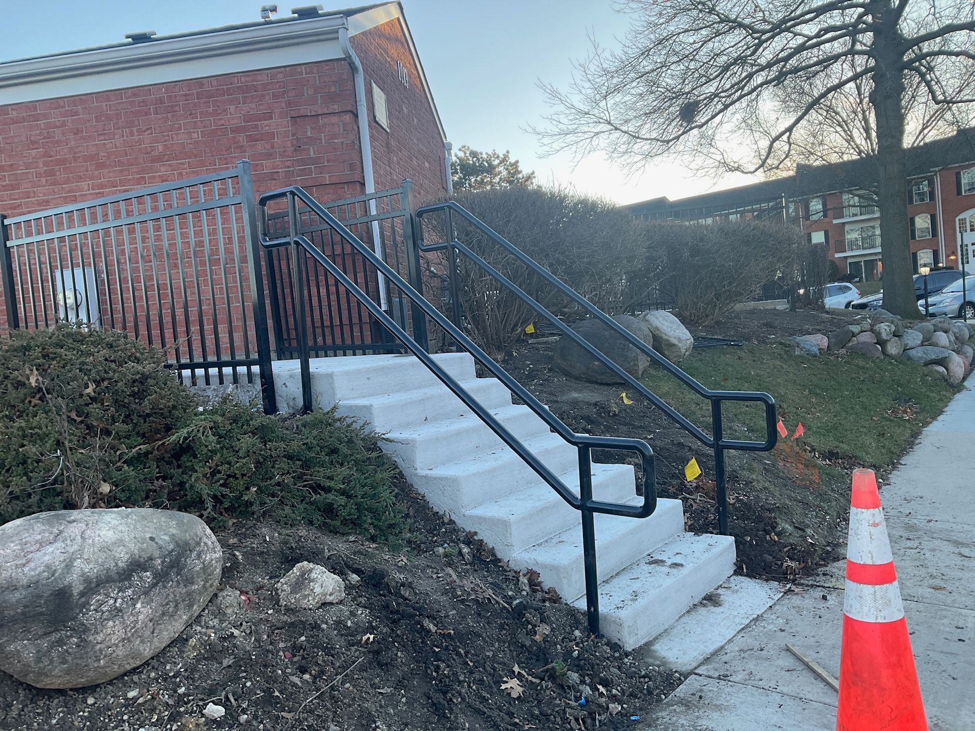 Concrete steps with black handrails leading up to a brick building.