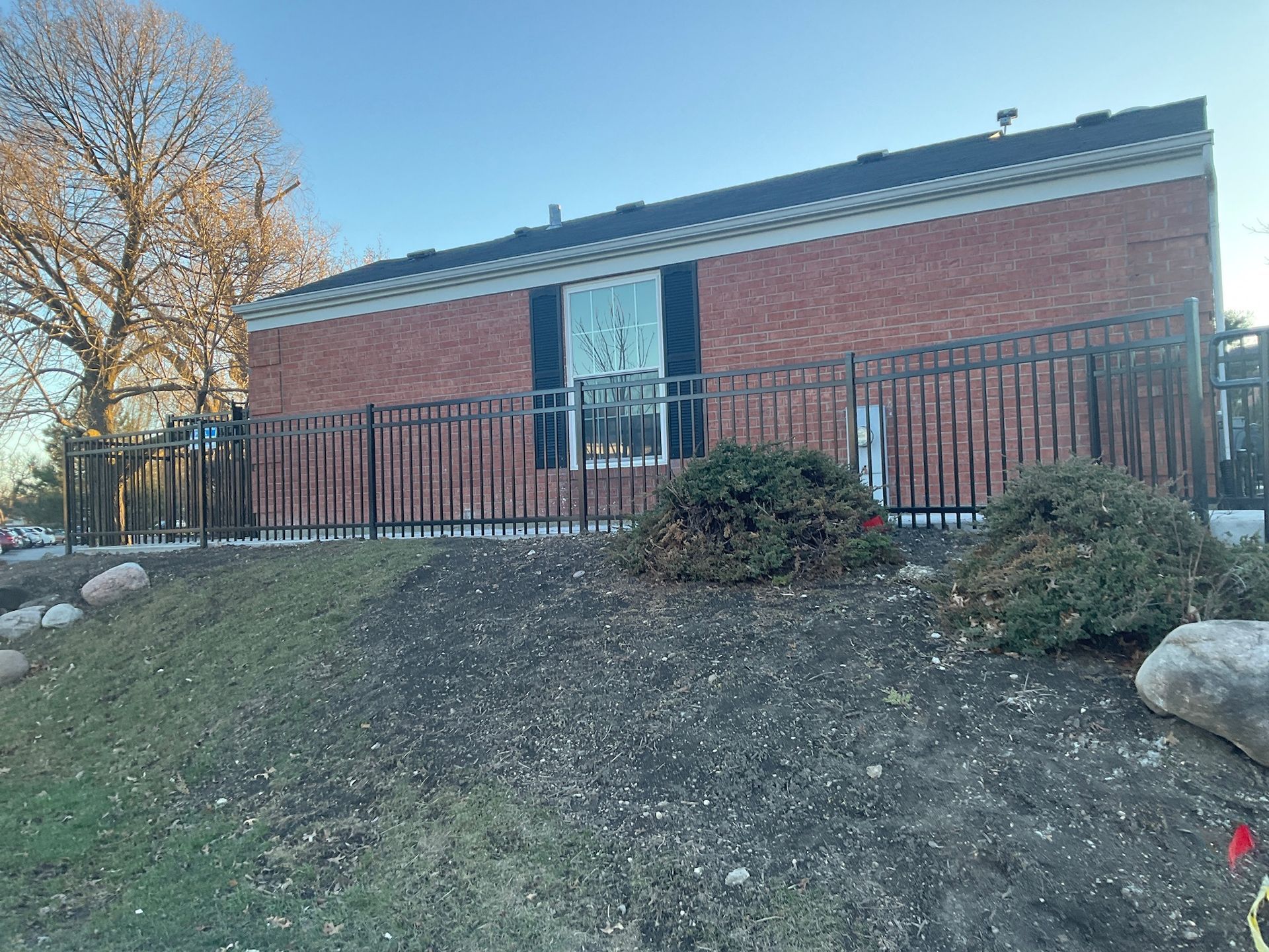 Red brick building with black fence, window, and small shrubs on a grassy hill.