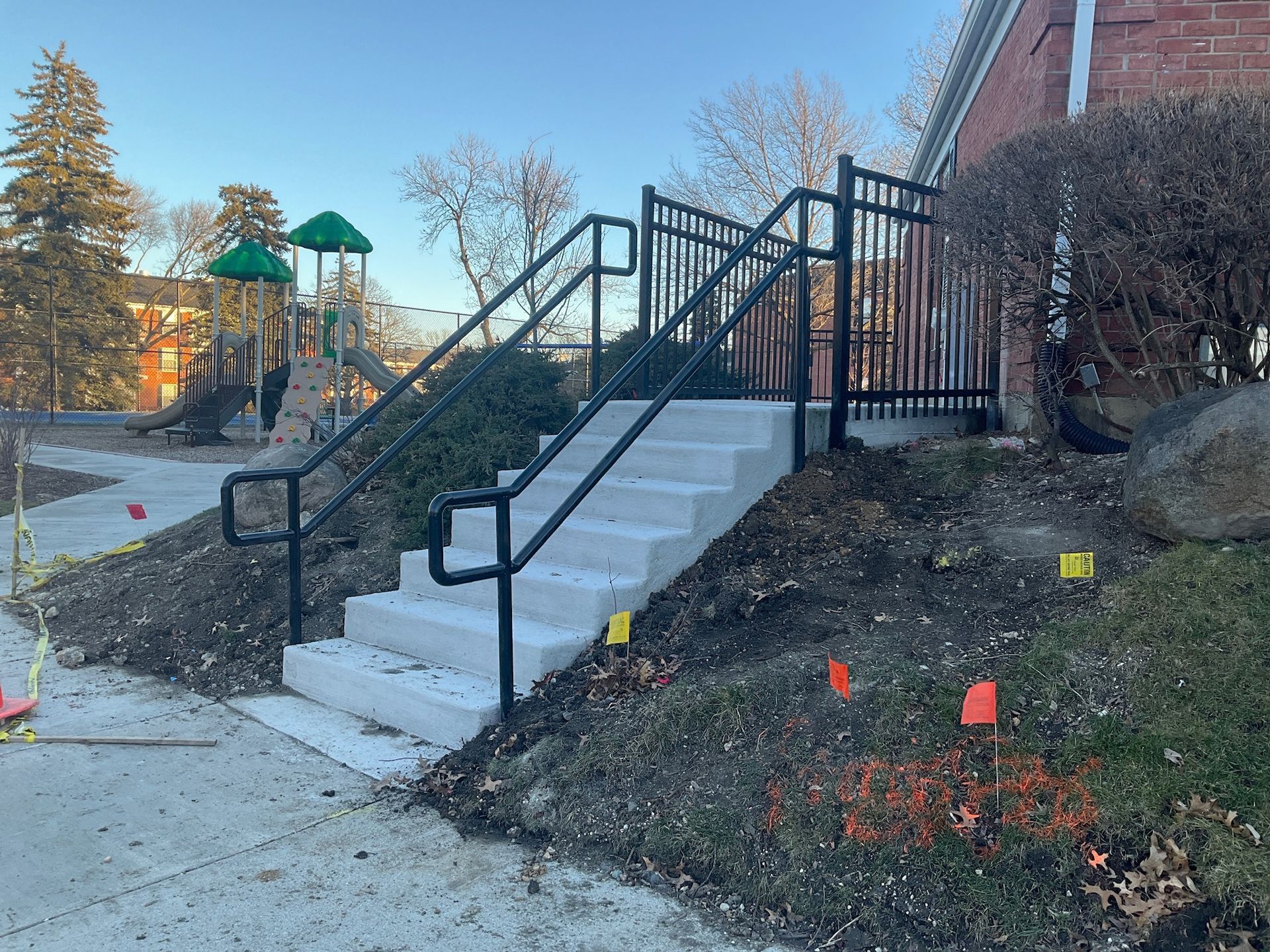 Concrete stairs with black handrails lead to a brick building. A playground is in the background.