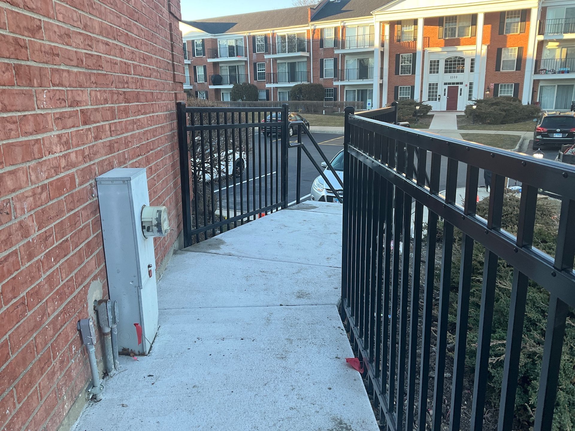 A brick building with a concrete walkway bordered by a black metal fence.