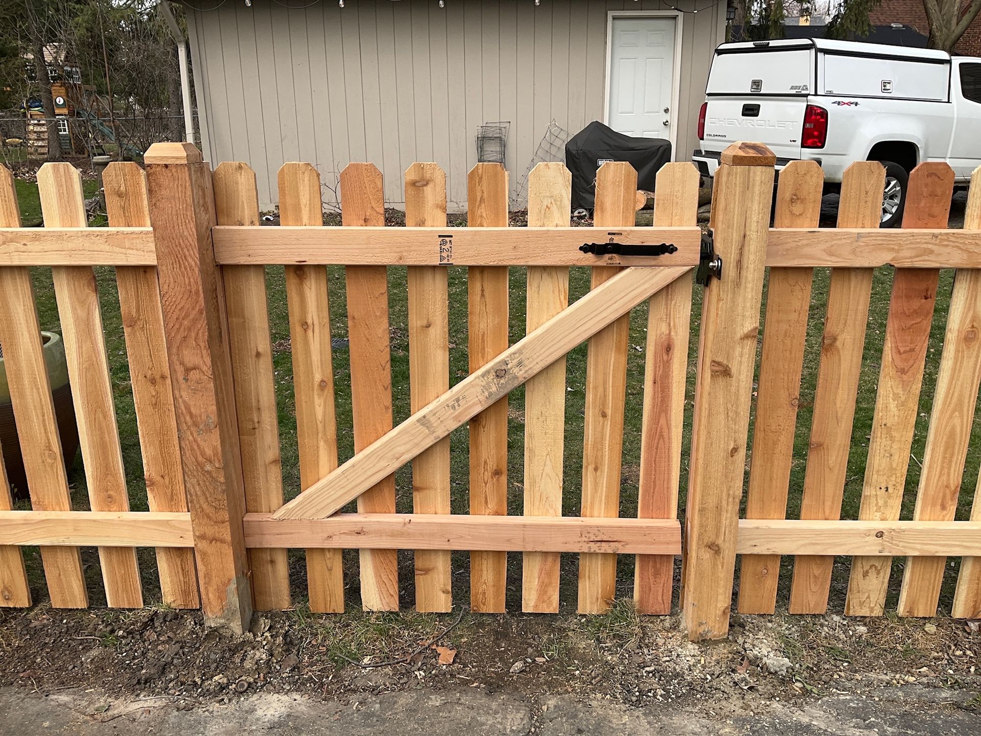 Wooden picket fence with gate; light brown, outdoors.