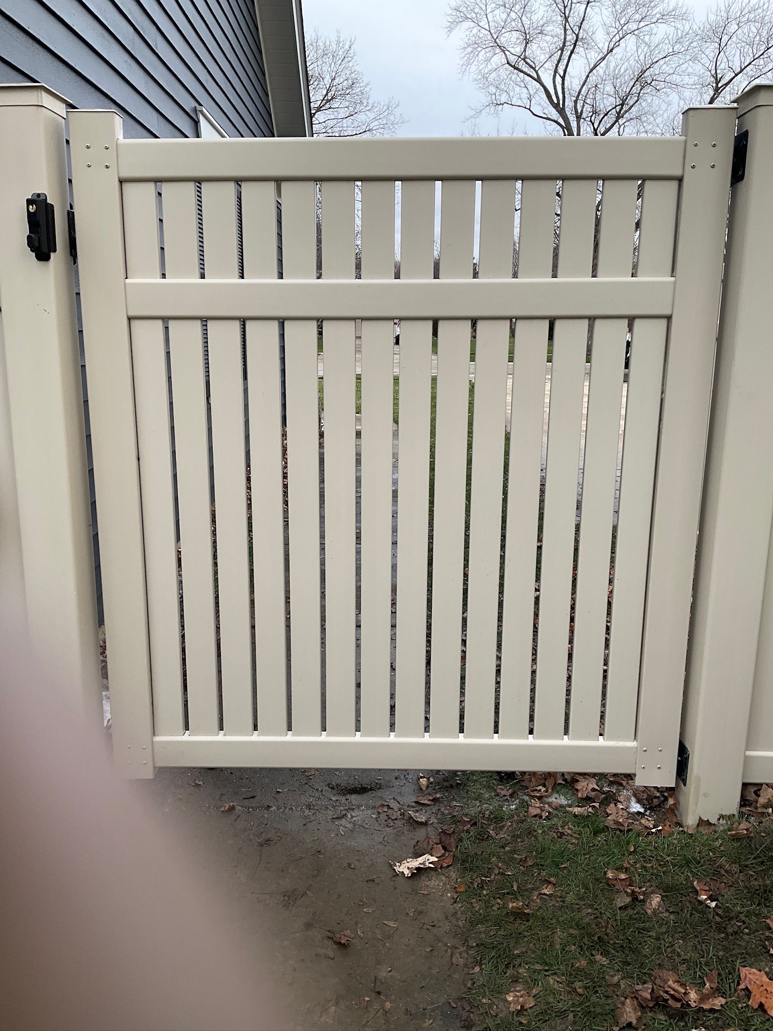 Tan vertical-slat fence gate, open, set in yard.