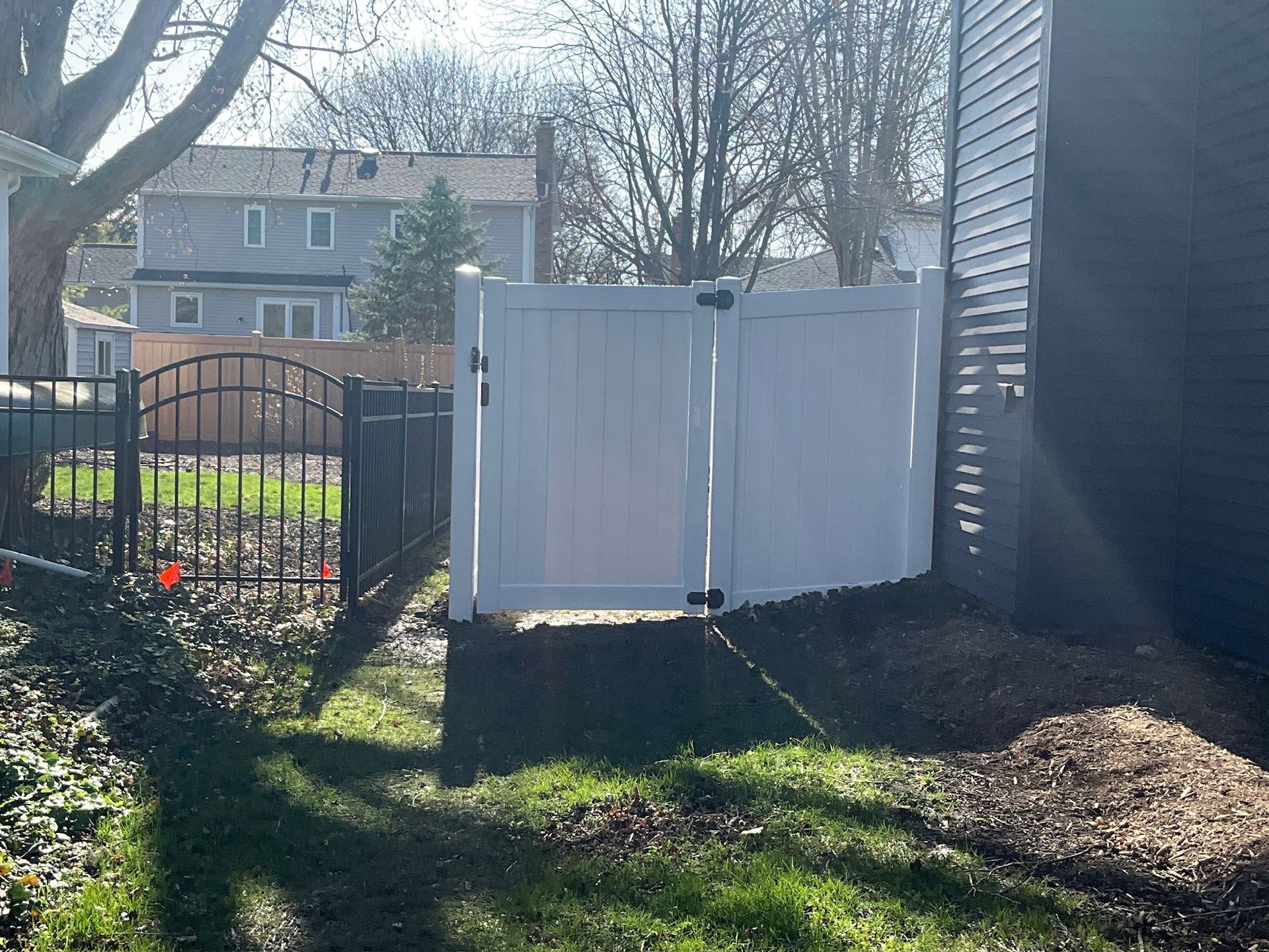 White privacy fence with double doors next to a dark house, and a black ornamental gate.