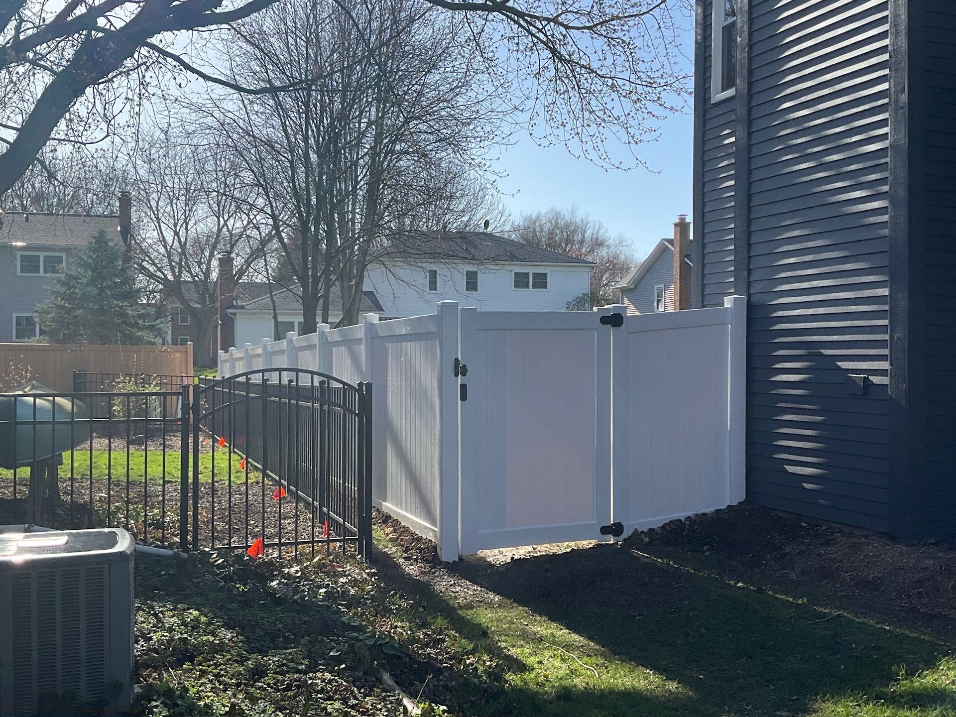 White privacy fence with black metal gate next to a house, on a sunny day.