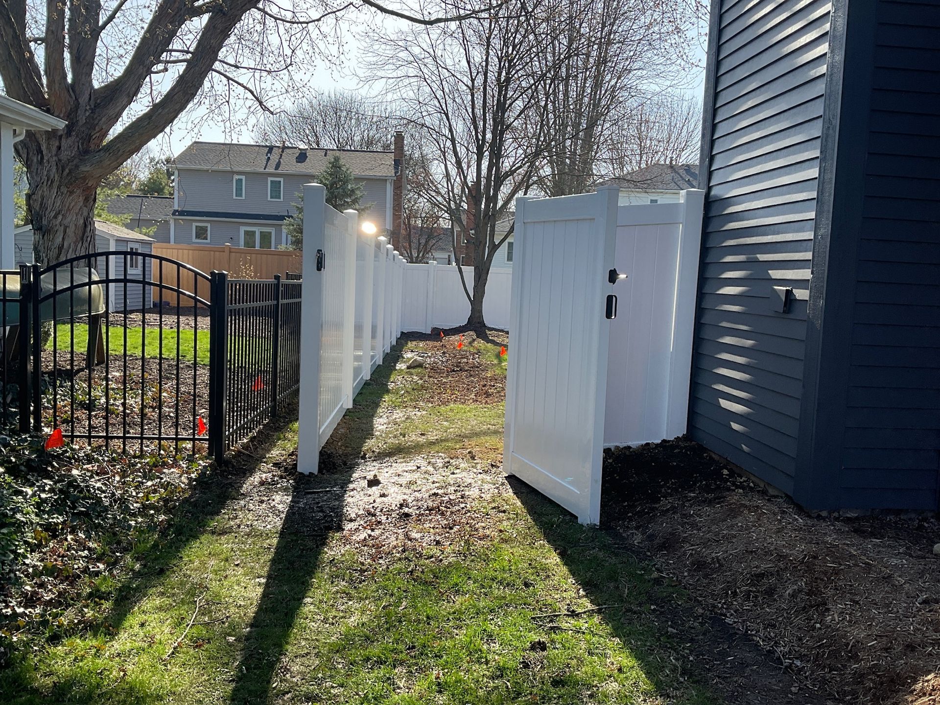 White vinyl fence with gate open, next to dark gray house.
