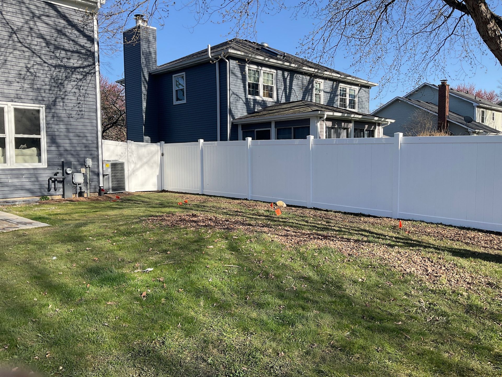 White vinyl fence encloses a grassy backyard with two-story blue house in the background.
