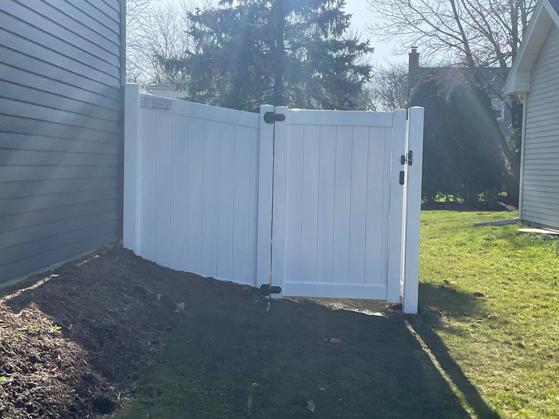 White vinyl fence gate in a backyard setting.
