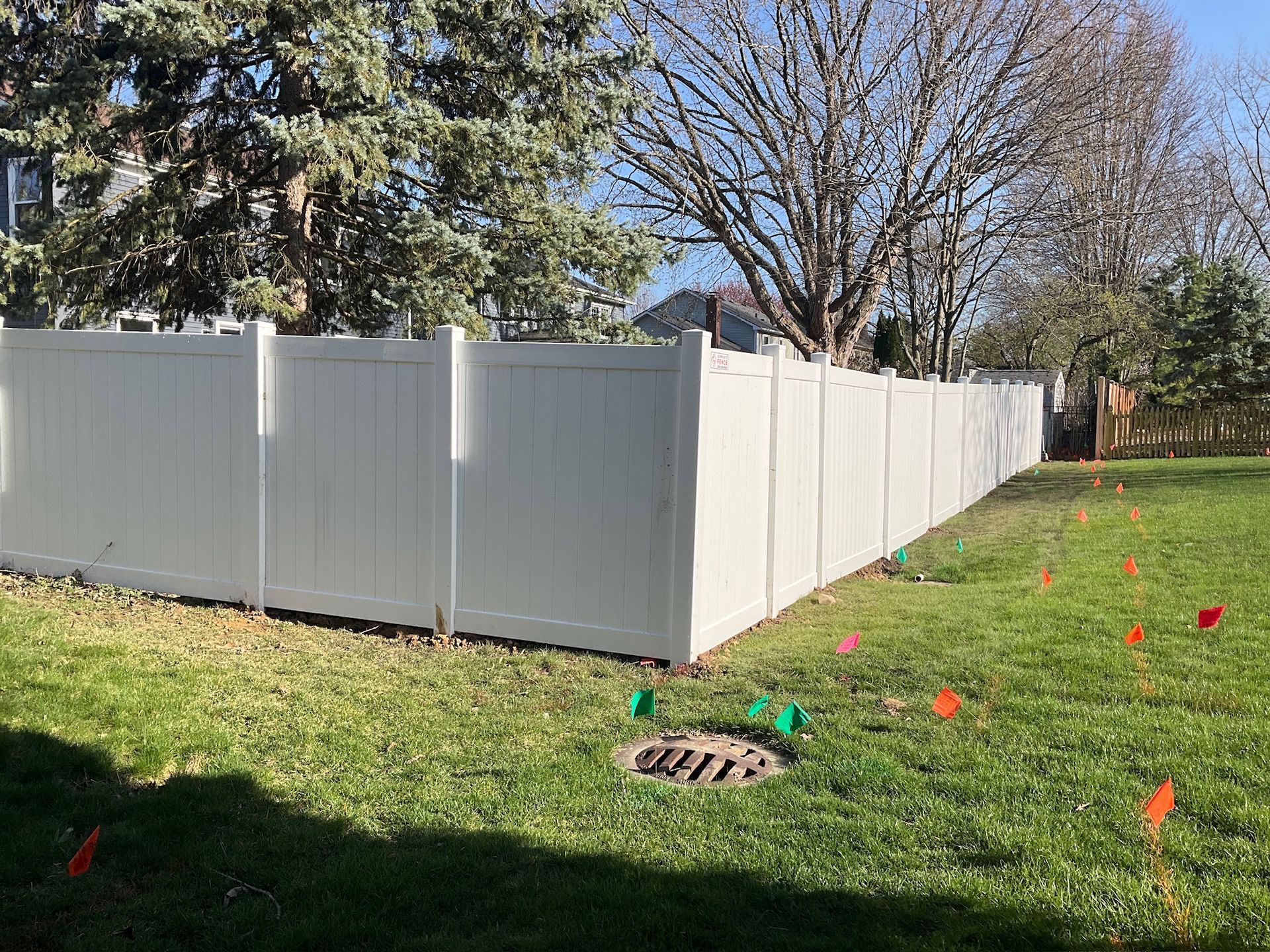 White vinyl fence in a grassy yard, with orange flags marking a line.