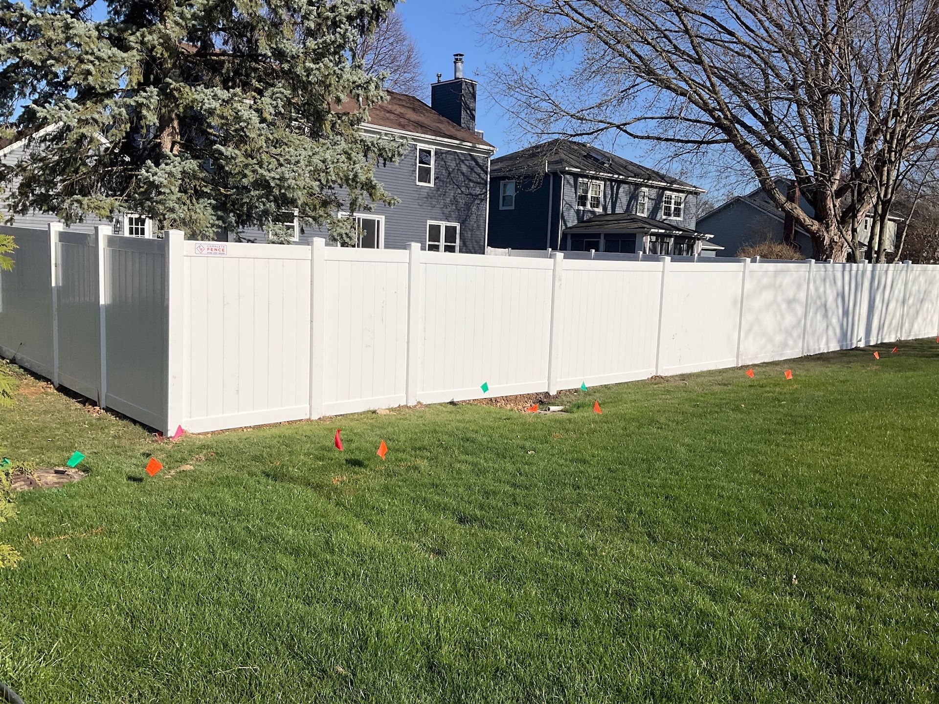 White vinyl fence in a grassy yard, with houses in the background under a blue sky.