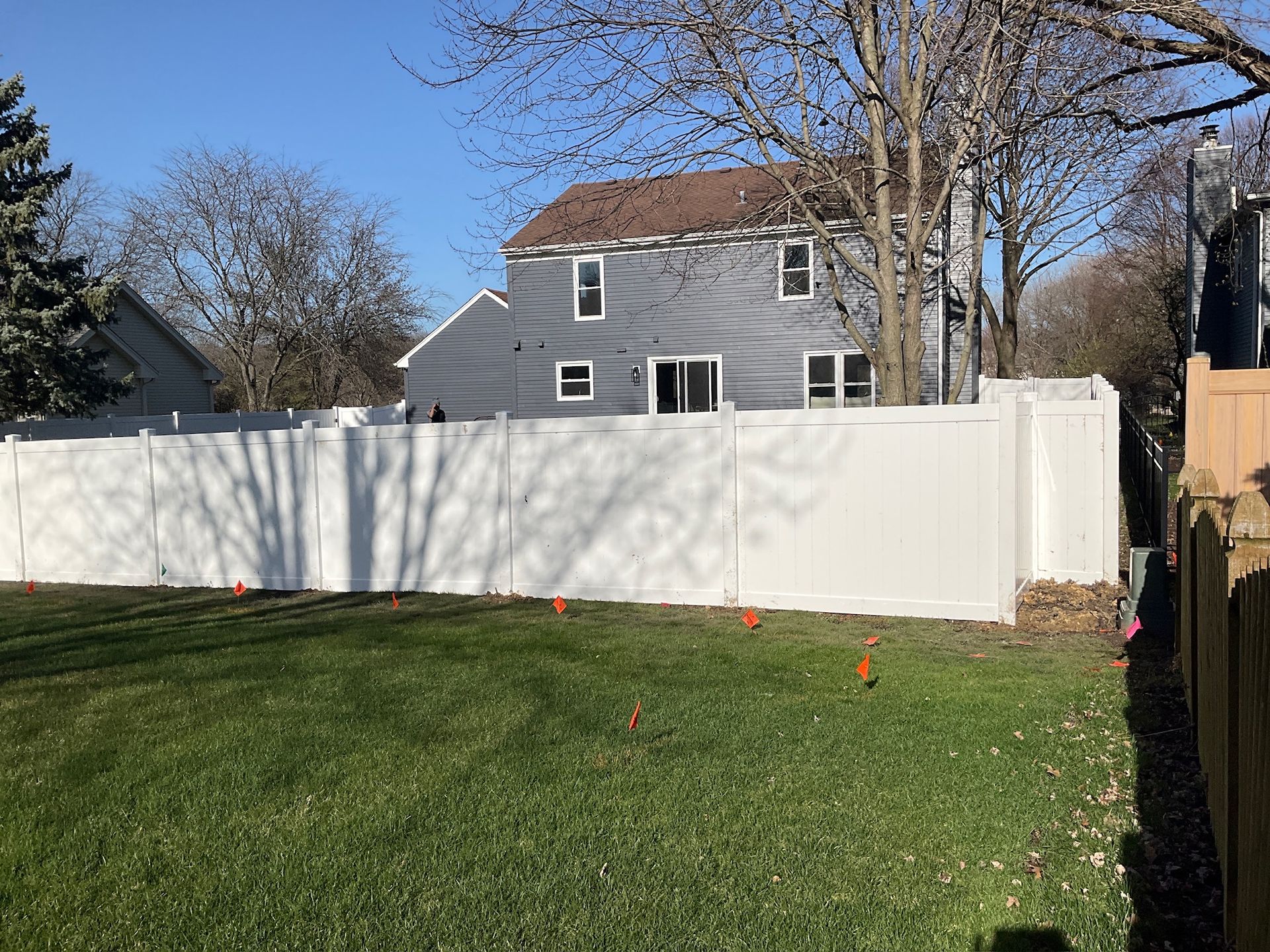 White fence in a grassy yard, with a gray house in the background and a blue sky.