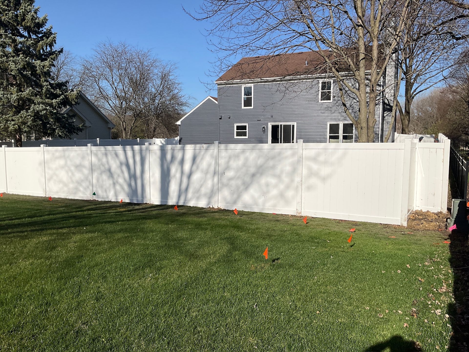 White vinyl fence enclosing a green lawn; gray house in the background.