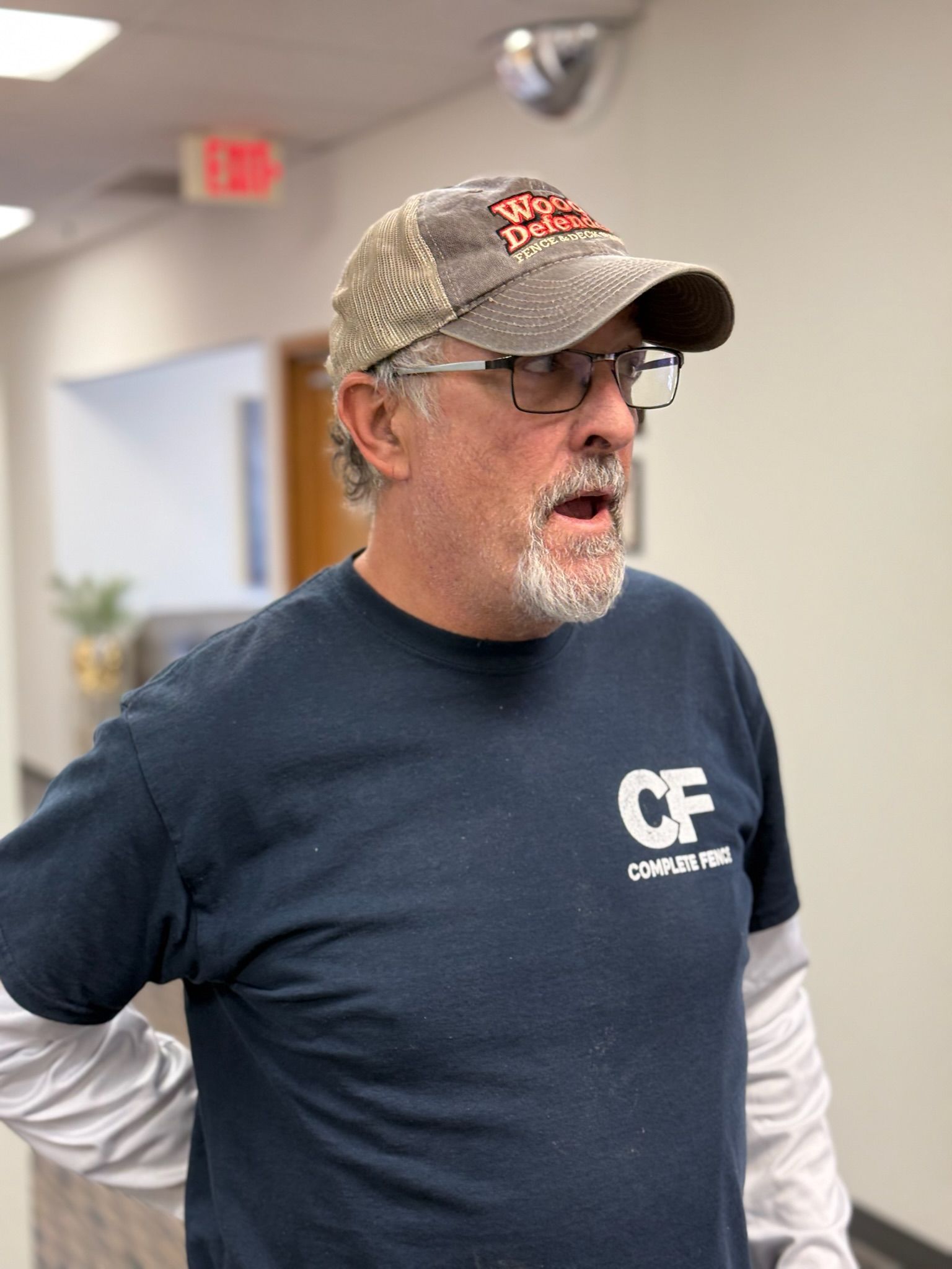 Man in a cap and glasses, wearing a blue shirt, looking to the side in a hallway.
