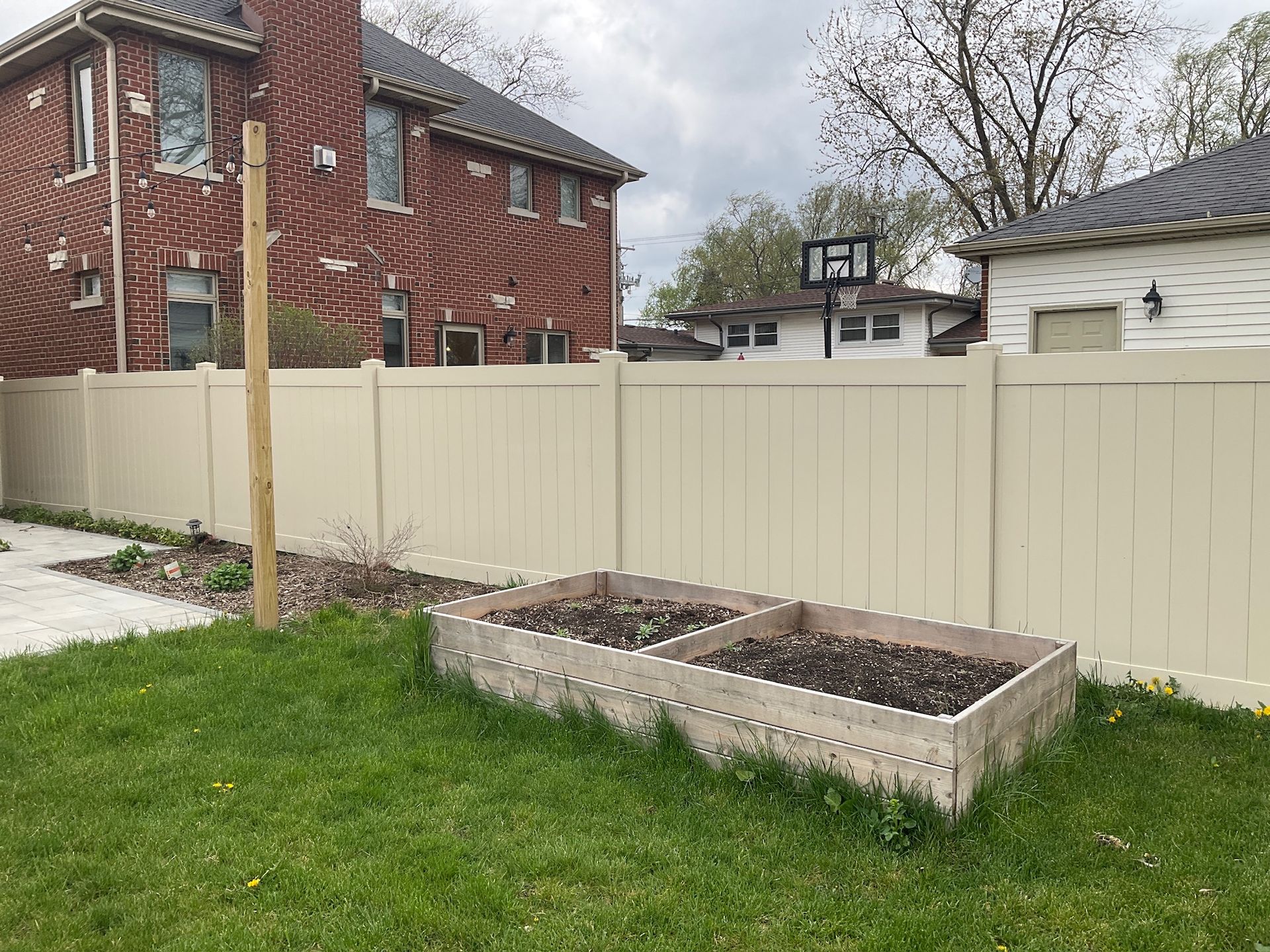Backyard with beige fence, raised garden bed, and brick house.