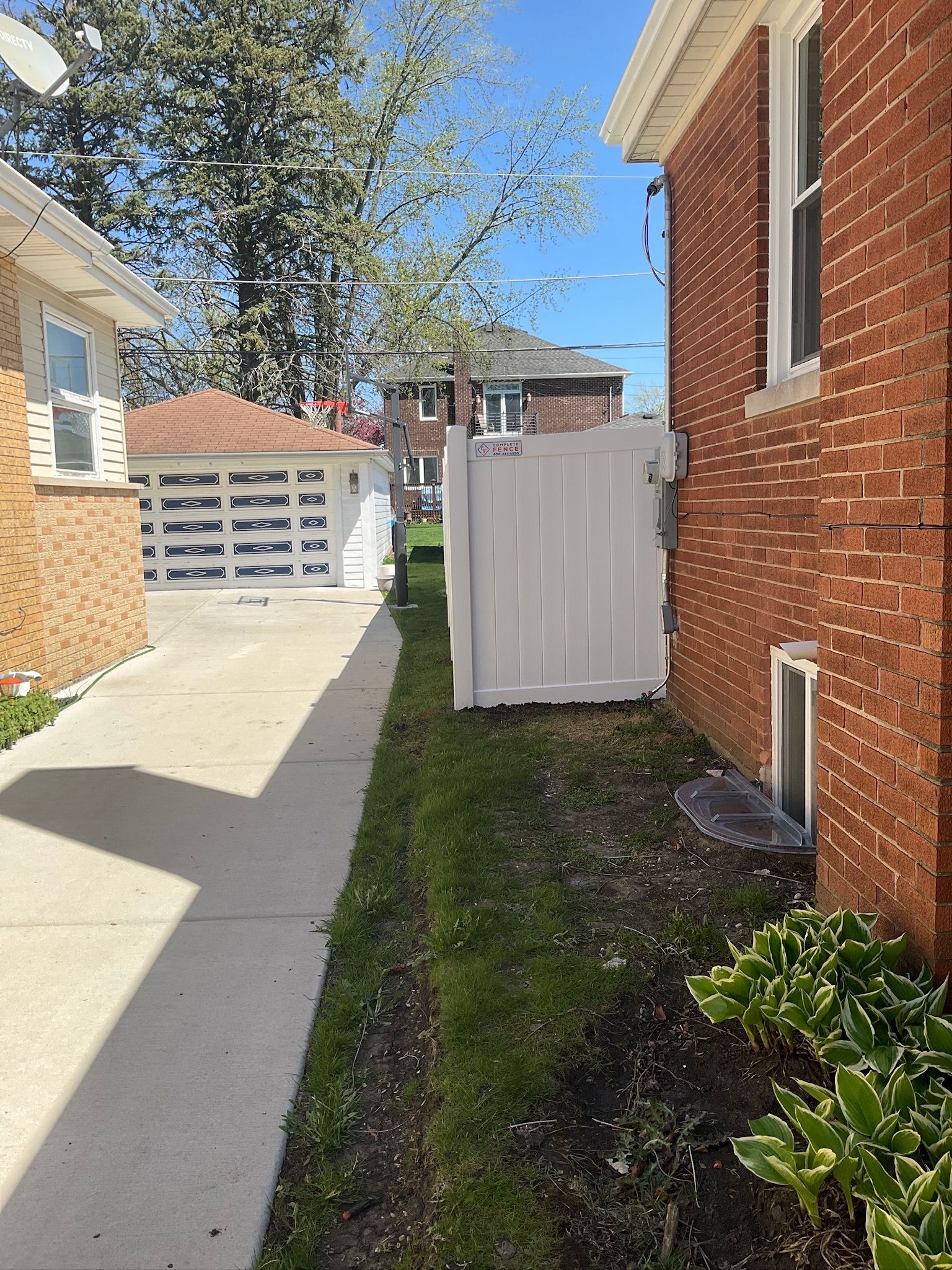 Narrow residential alley with brick house on right, white fence and garage on left, green grass.