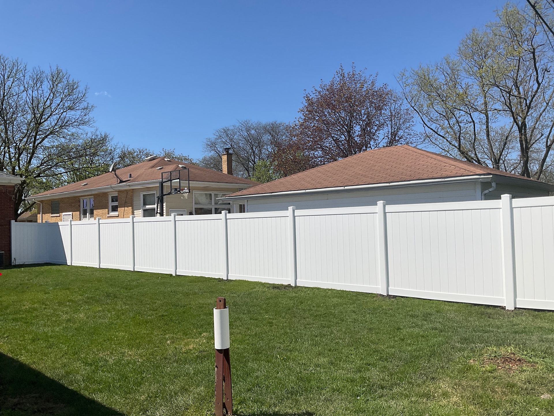 White vinyl fence along green lawn, with houses and blue sky in background.
