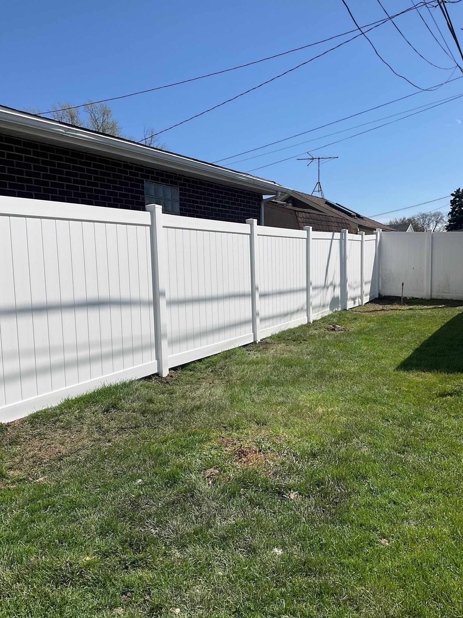 White vinyl fence in a grassy yard, with a brick building in the background.
