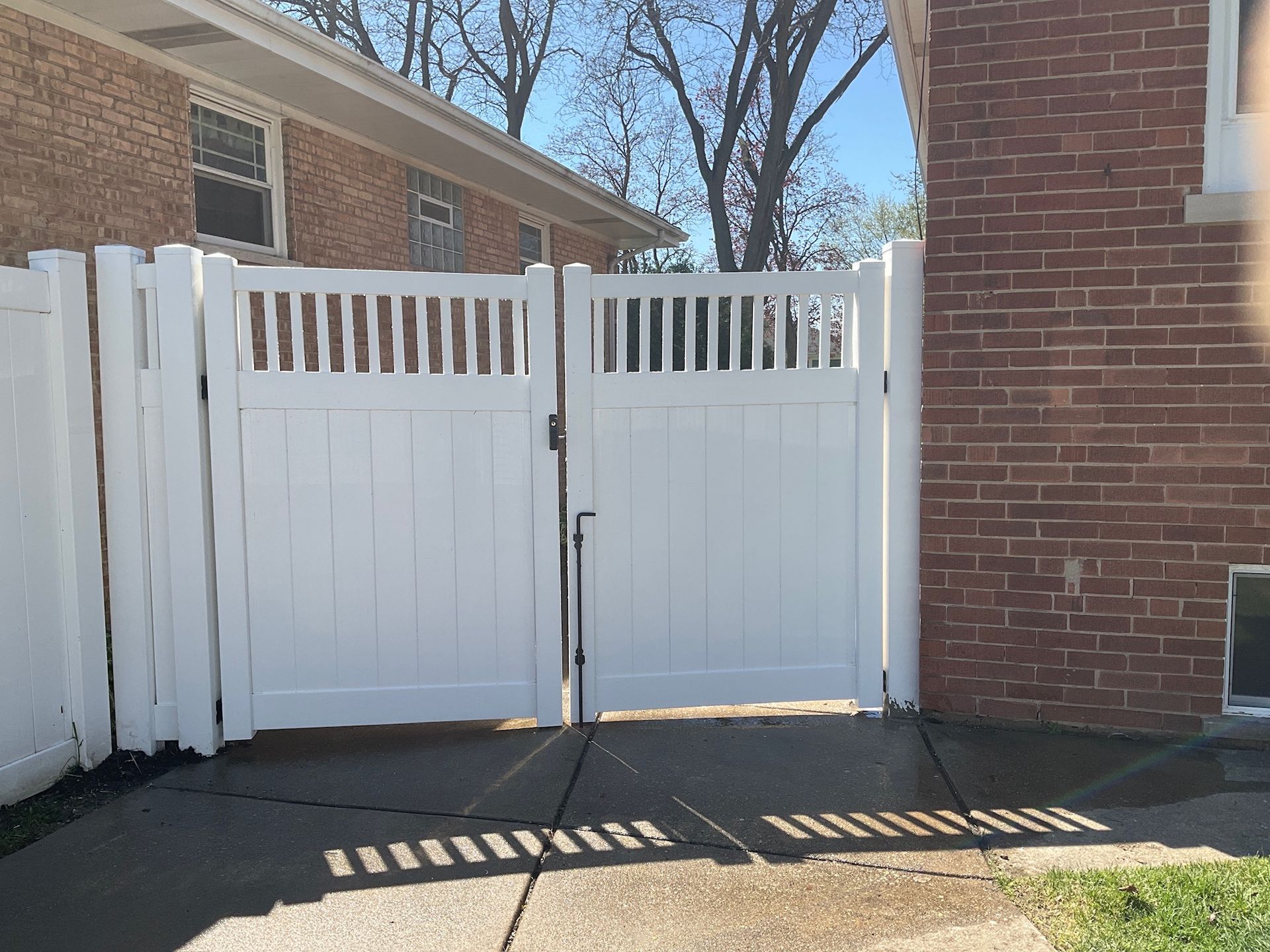 White vinyl fence with gate, set against a brick building, sunny day.
