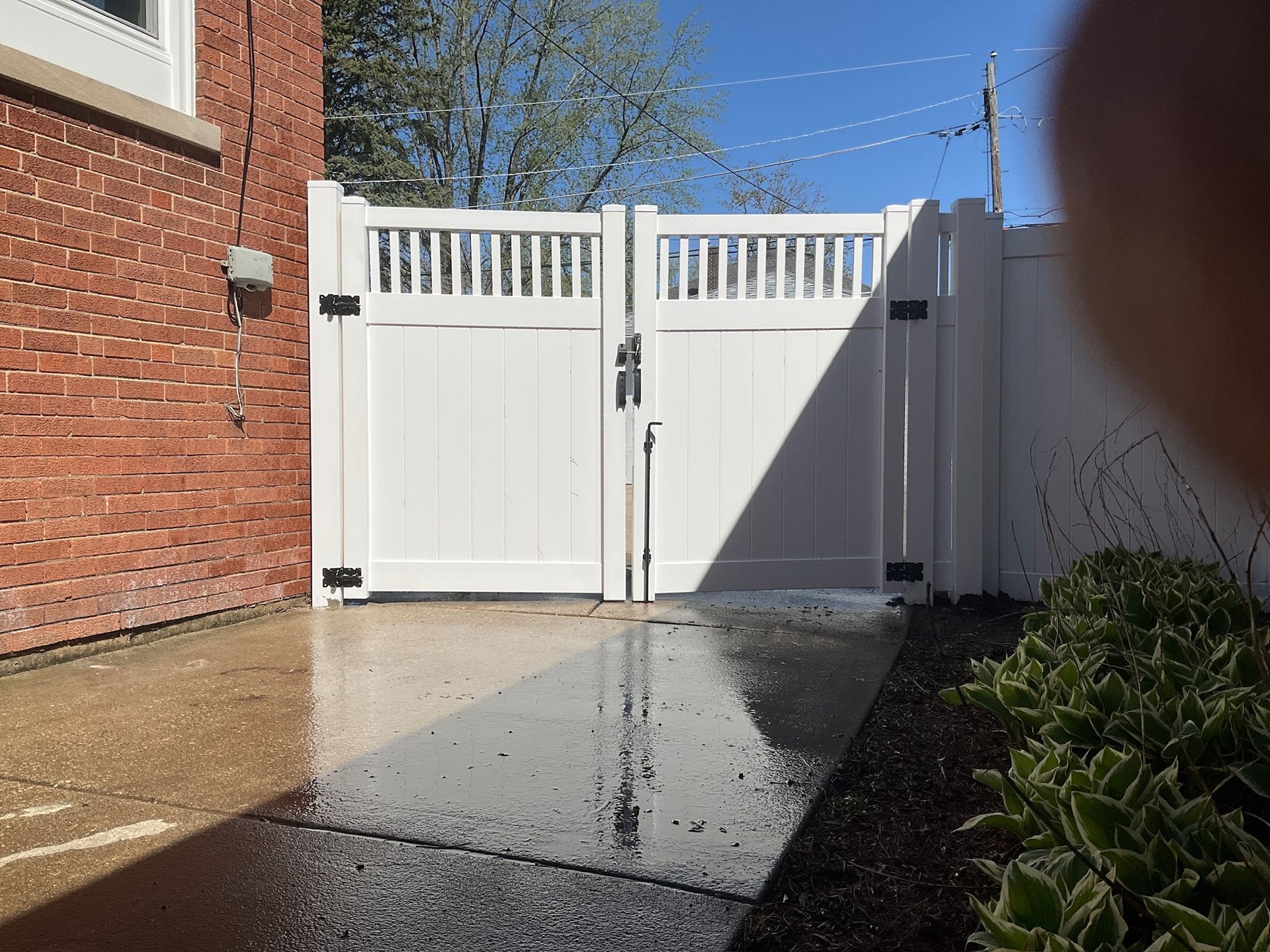 White double gate in a white fence. Brick building to the left, blue sky.
