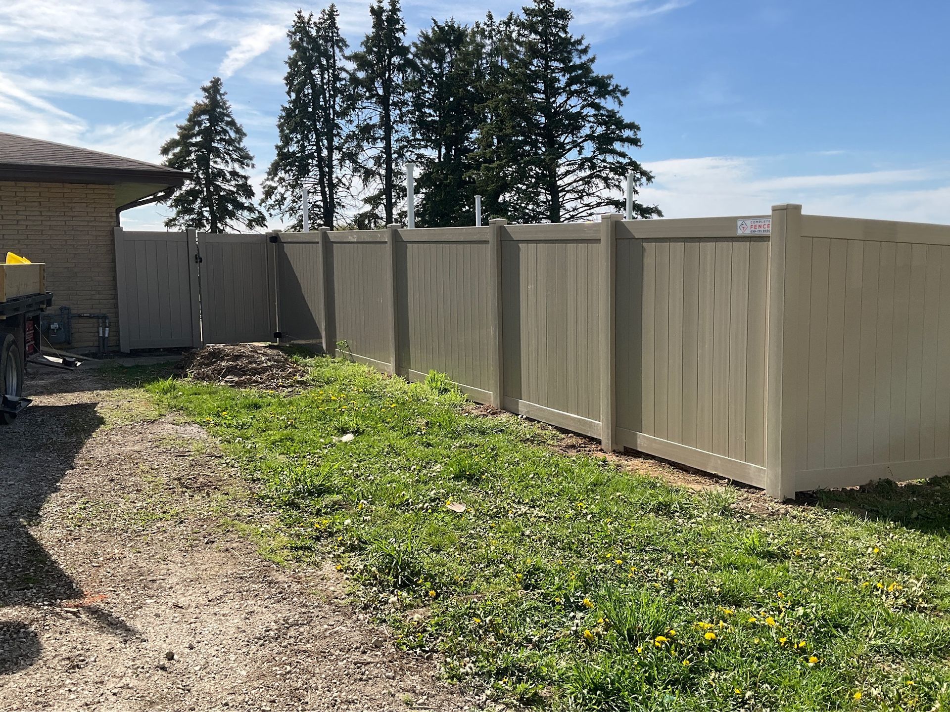 Beige privacy fence borders a grassy area next to a building on a sunny day.