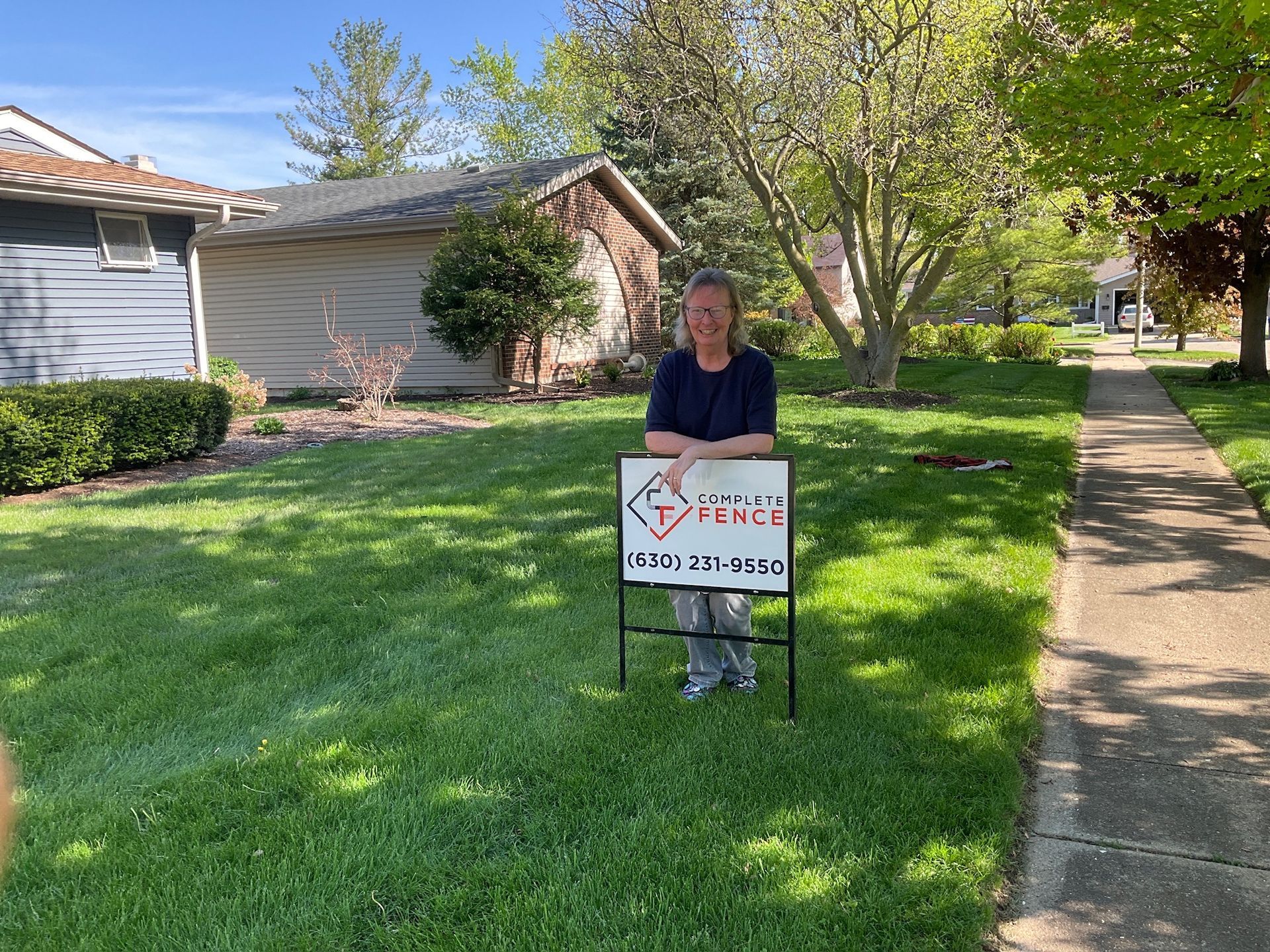 Woman standing next to a real estate sign in front of a house, sunny day.
