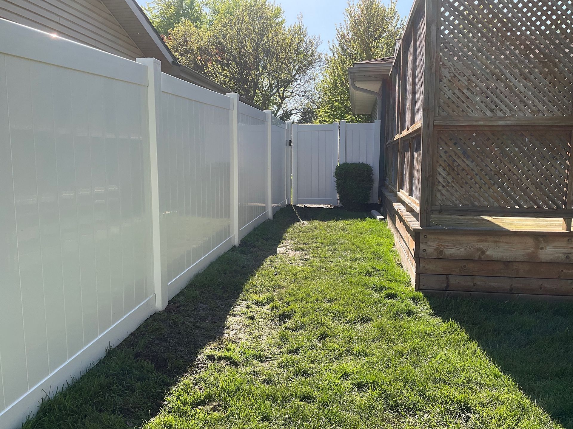 White vinyl fence with a gate, next to a grassy lawn and a wooden structure.