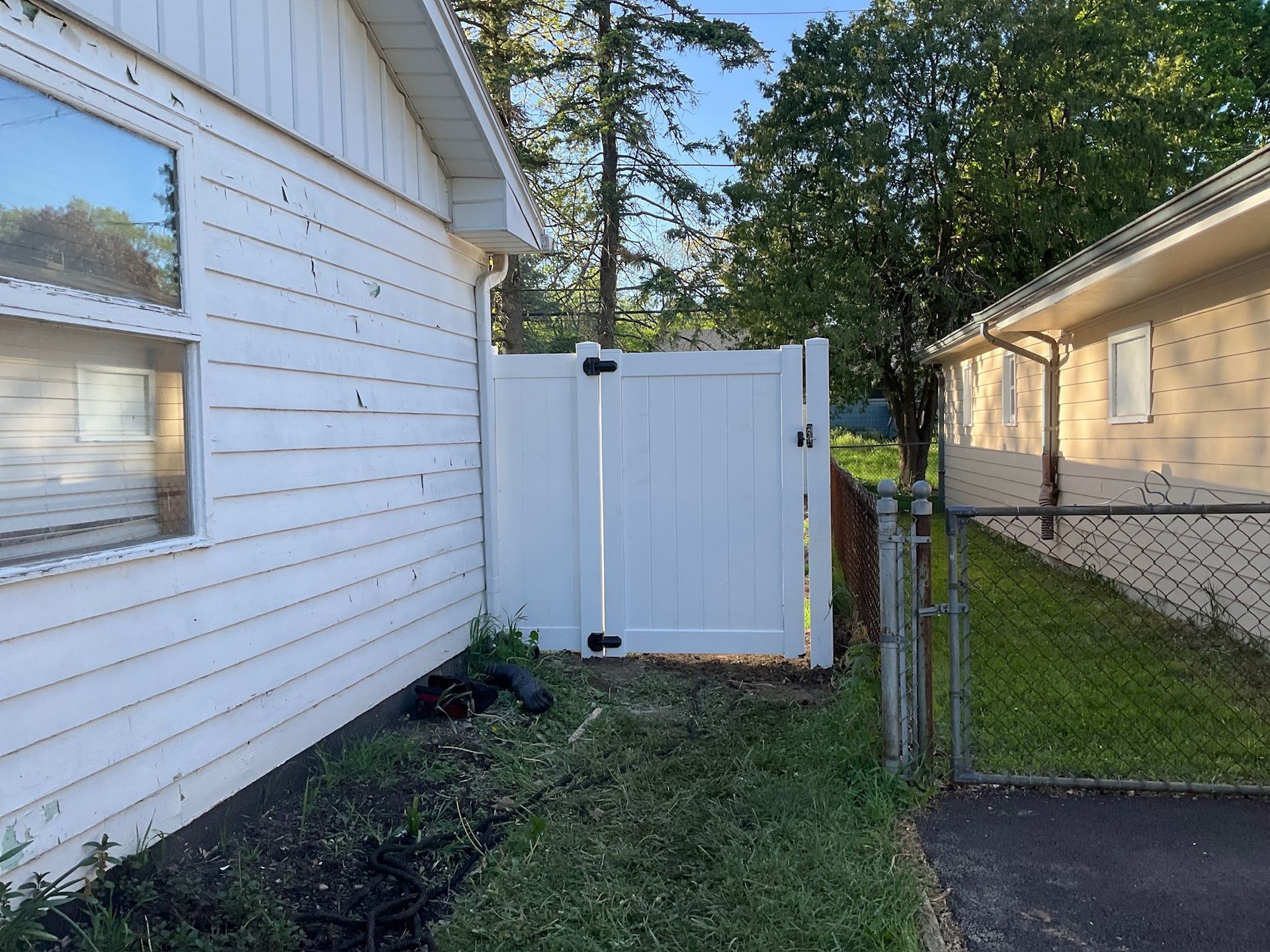 White privacy fence between two houses, with a chain-link fence on the right.