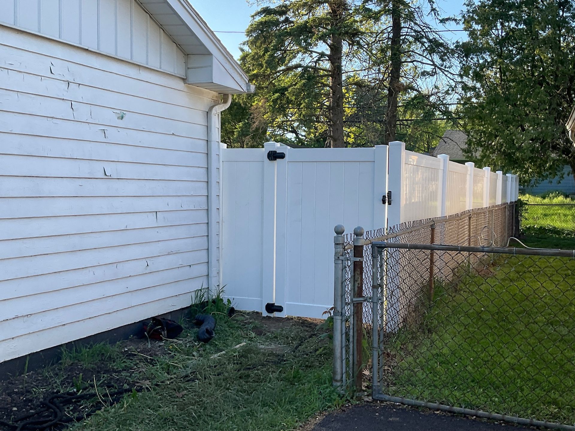 White vinyl gate and fence attached to a house and chain-link fence.