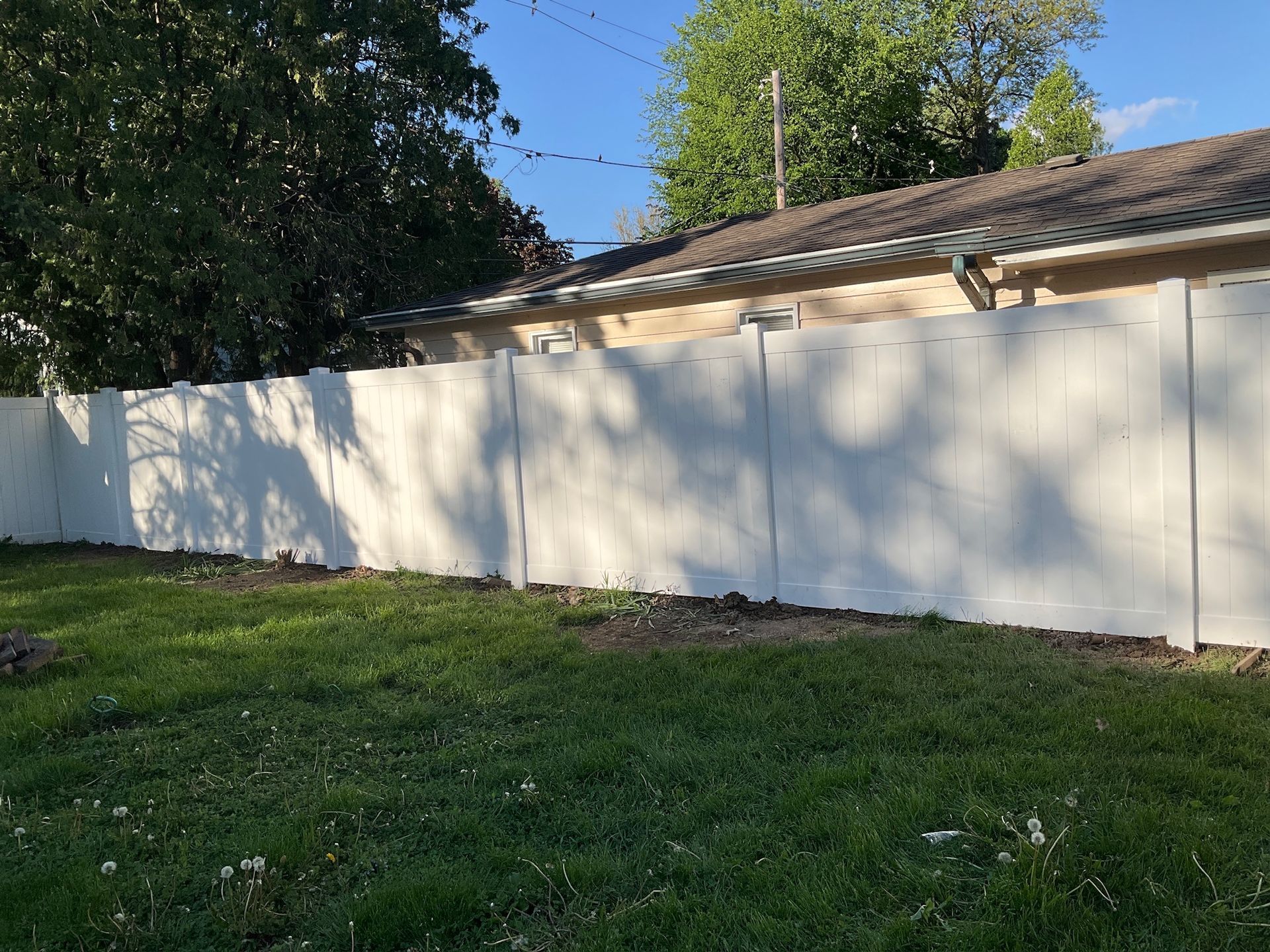 White privacy fence in a grassy yard, with a building and trees in the background under a blue sky.