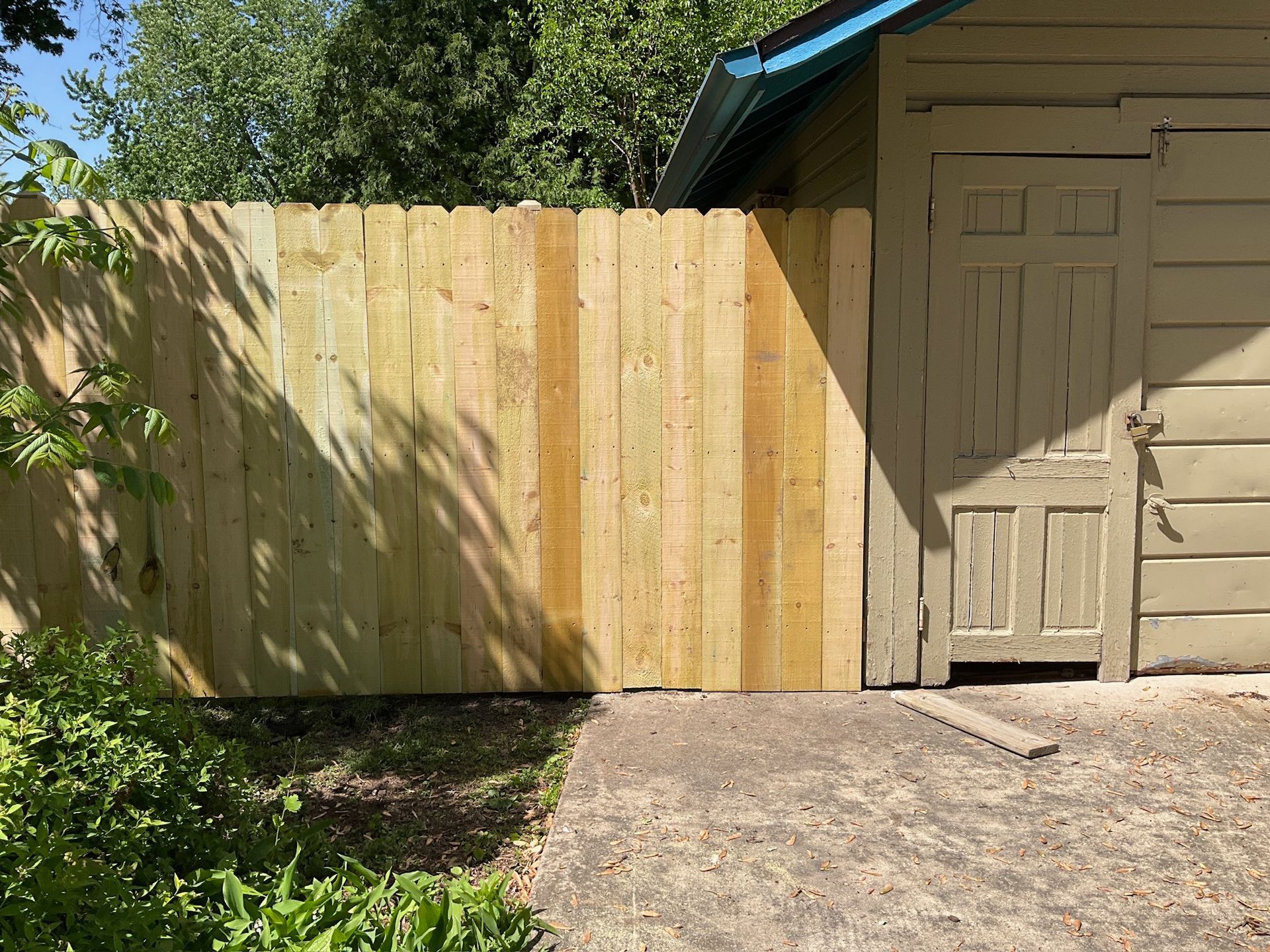 Wooden fence next to a weathered beige shed with a closed door, outdoors.