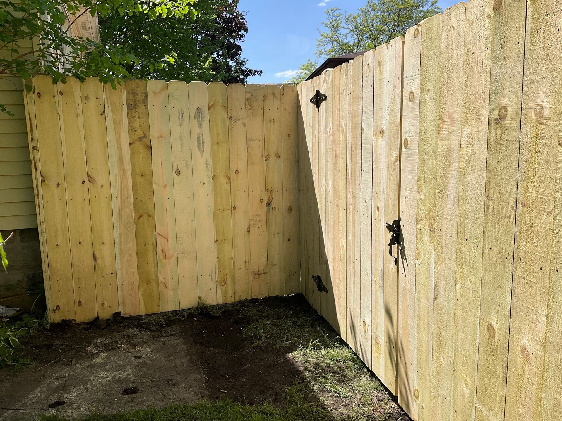 Wooden fence corner, natural wood color, in a yard with grass and blue sky visible.