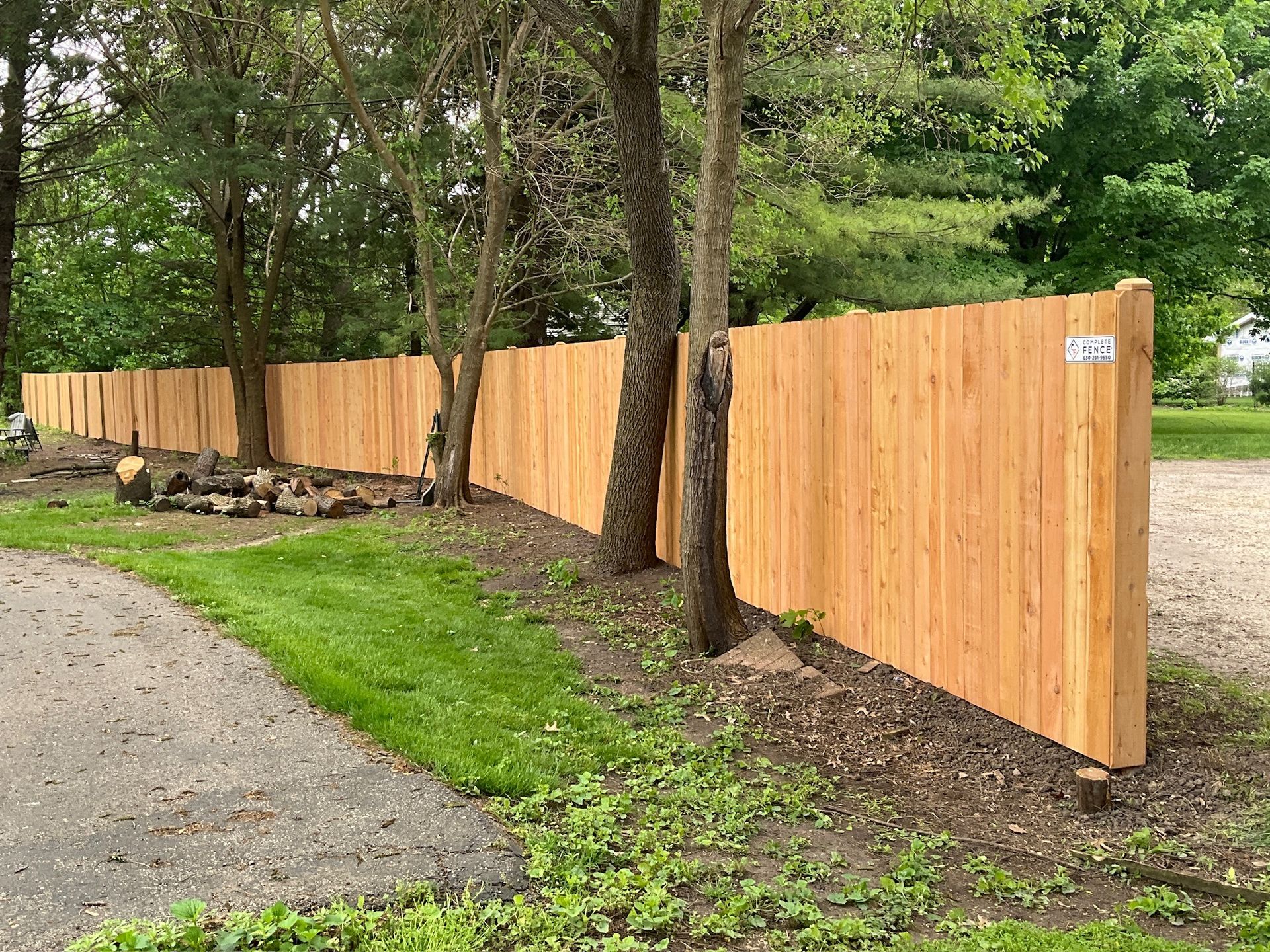Wooden fence bordering green grass and trees along a paved path.
