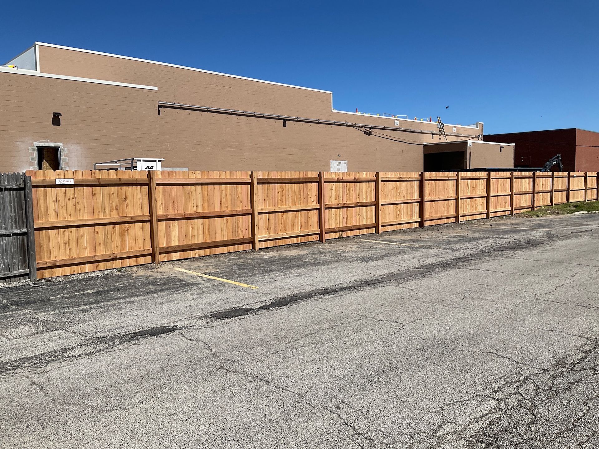 Wooden fence in front of a tan building under a blue sky, gravel parking area in the foreground.