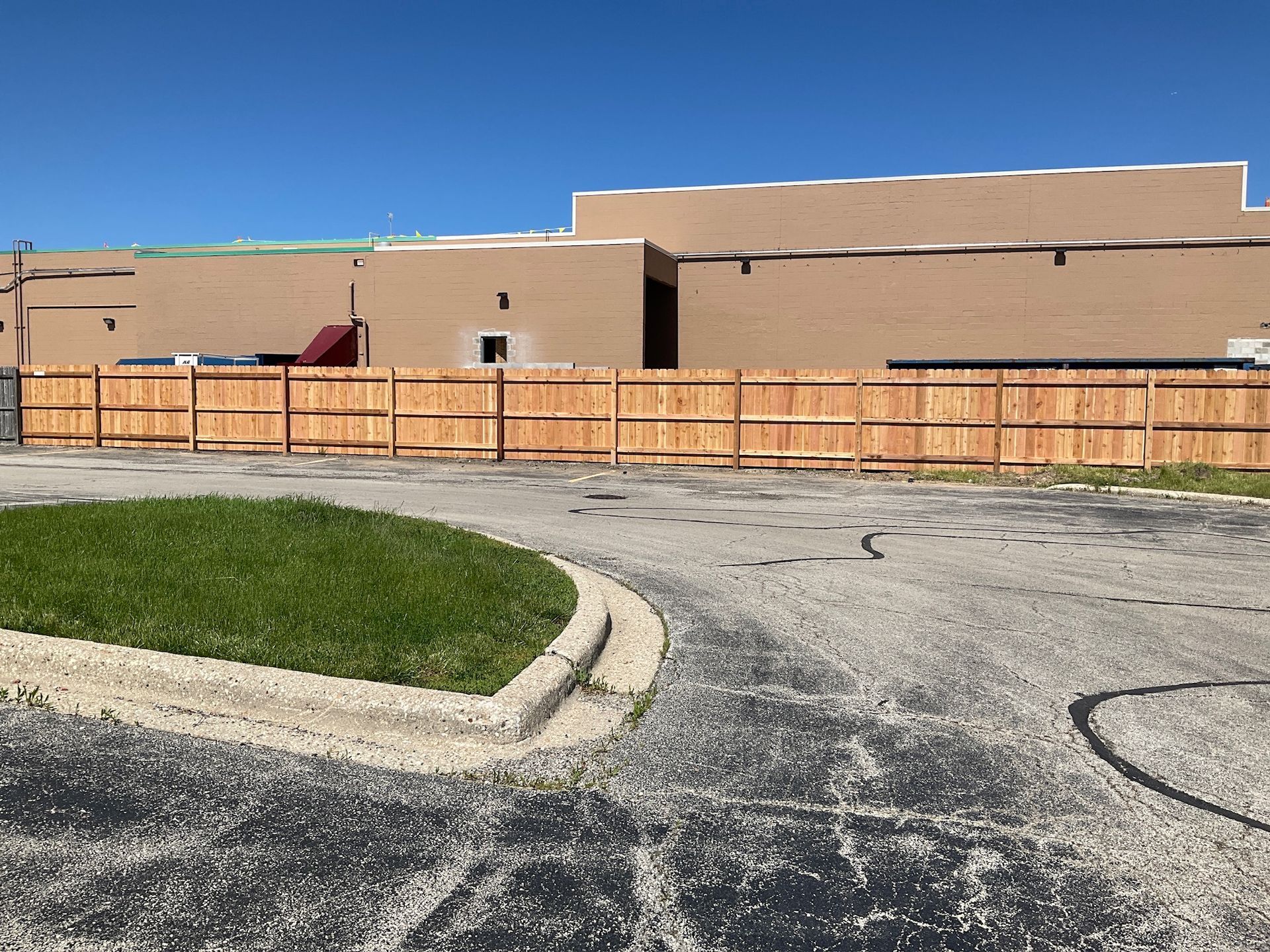 A wooden fence in front of a tan building; a small patch of green grass is in the foreground.