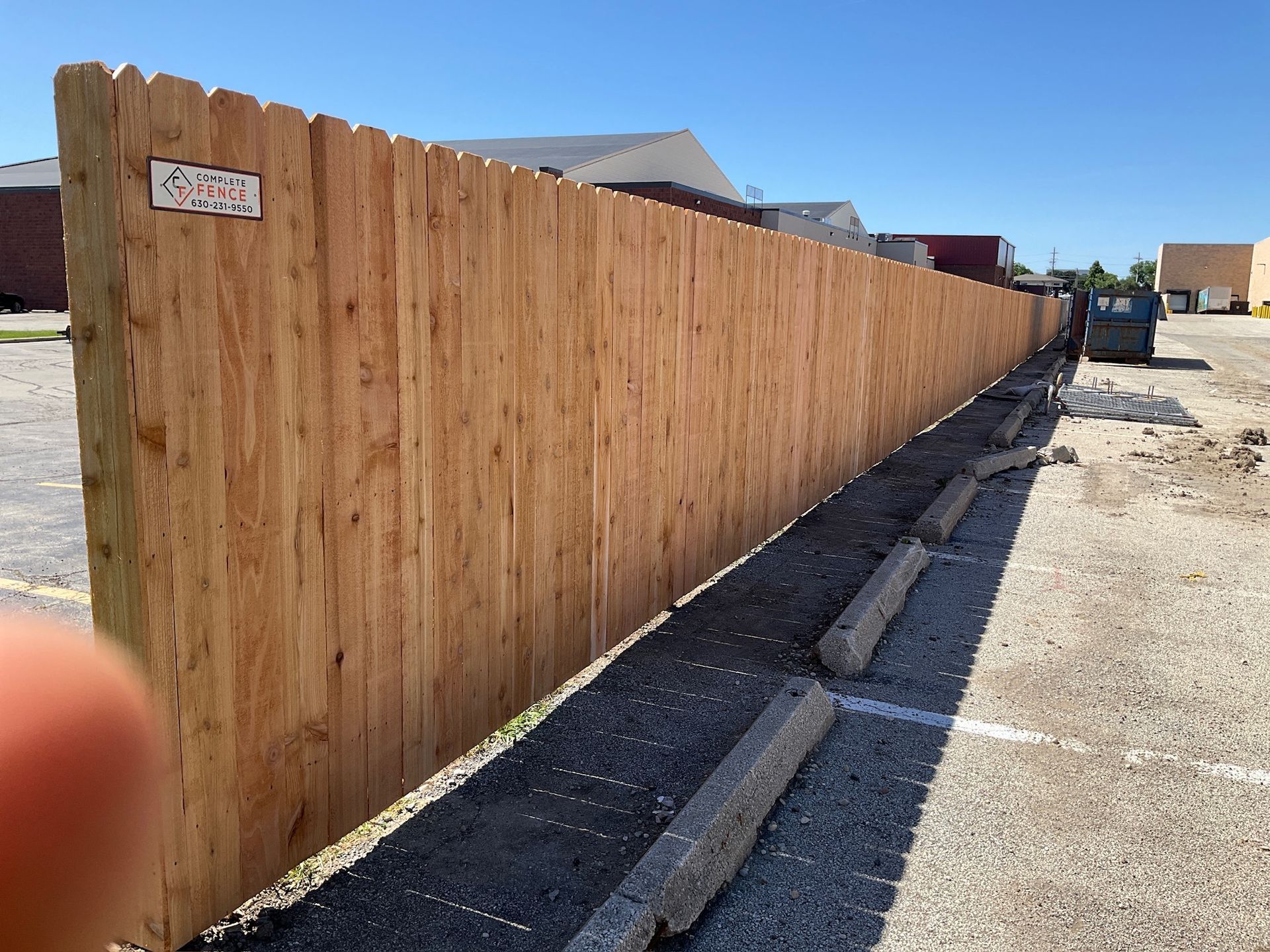 A long wooden fence in a parking lot on a sunny day.