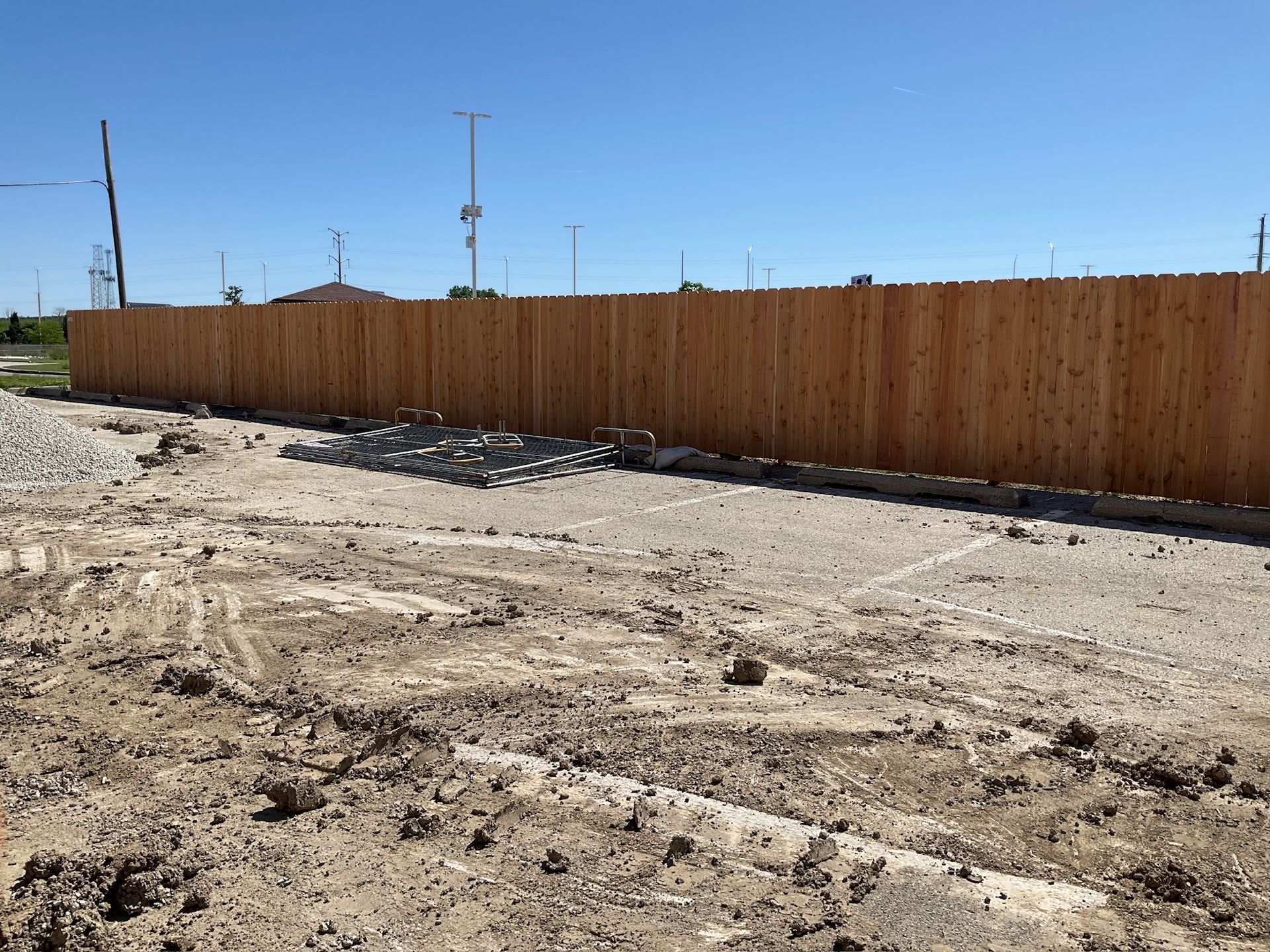 Dirt lot with a wooden fence. Scattered rocks and a clear blue sky.