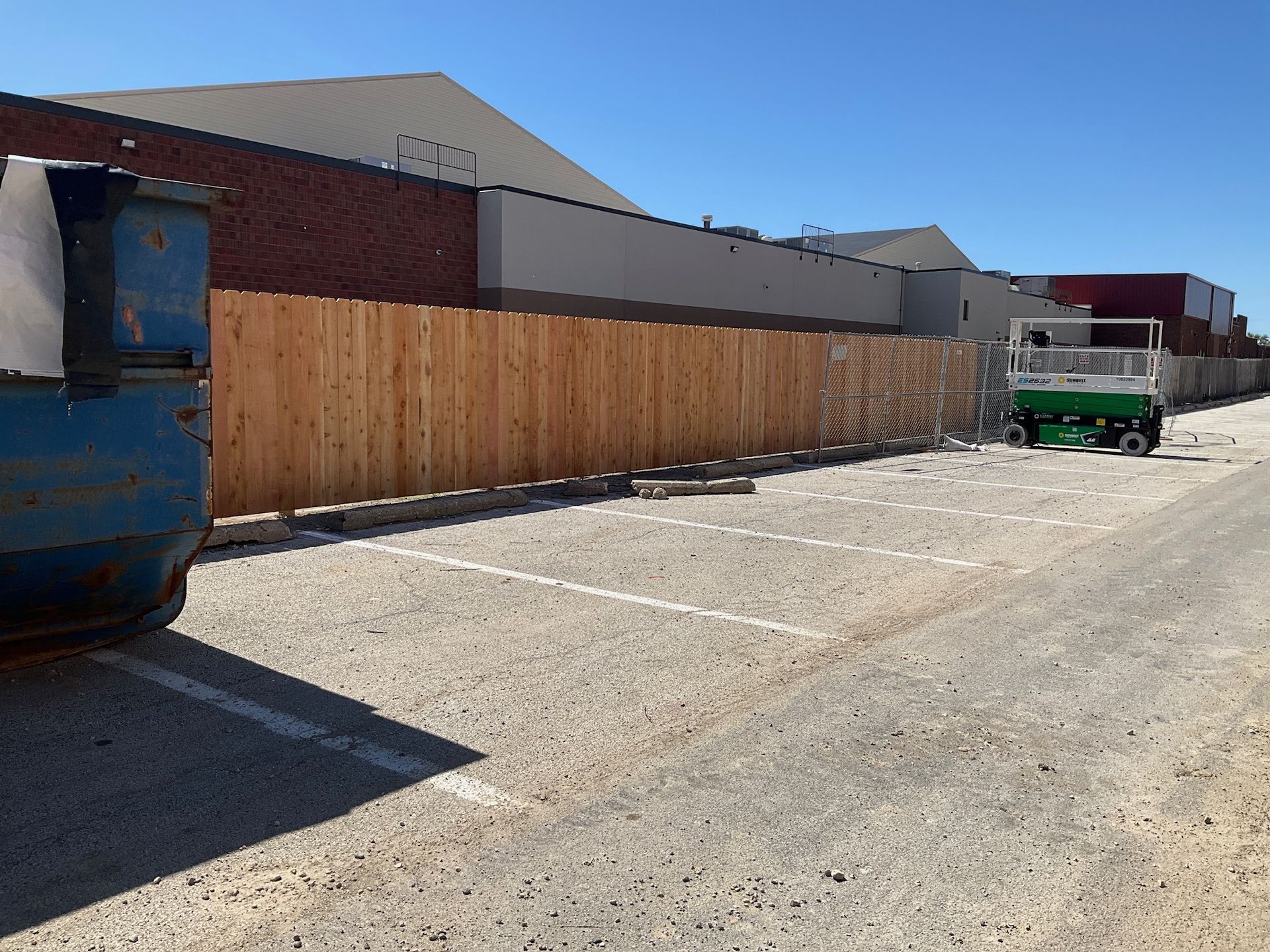 Parking lot with wooden fence and dumpster. Lift equipment visible.