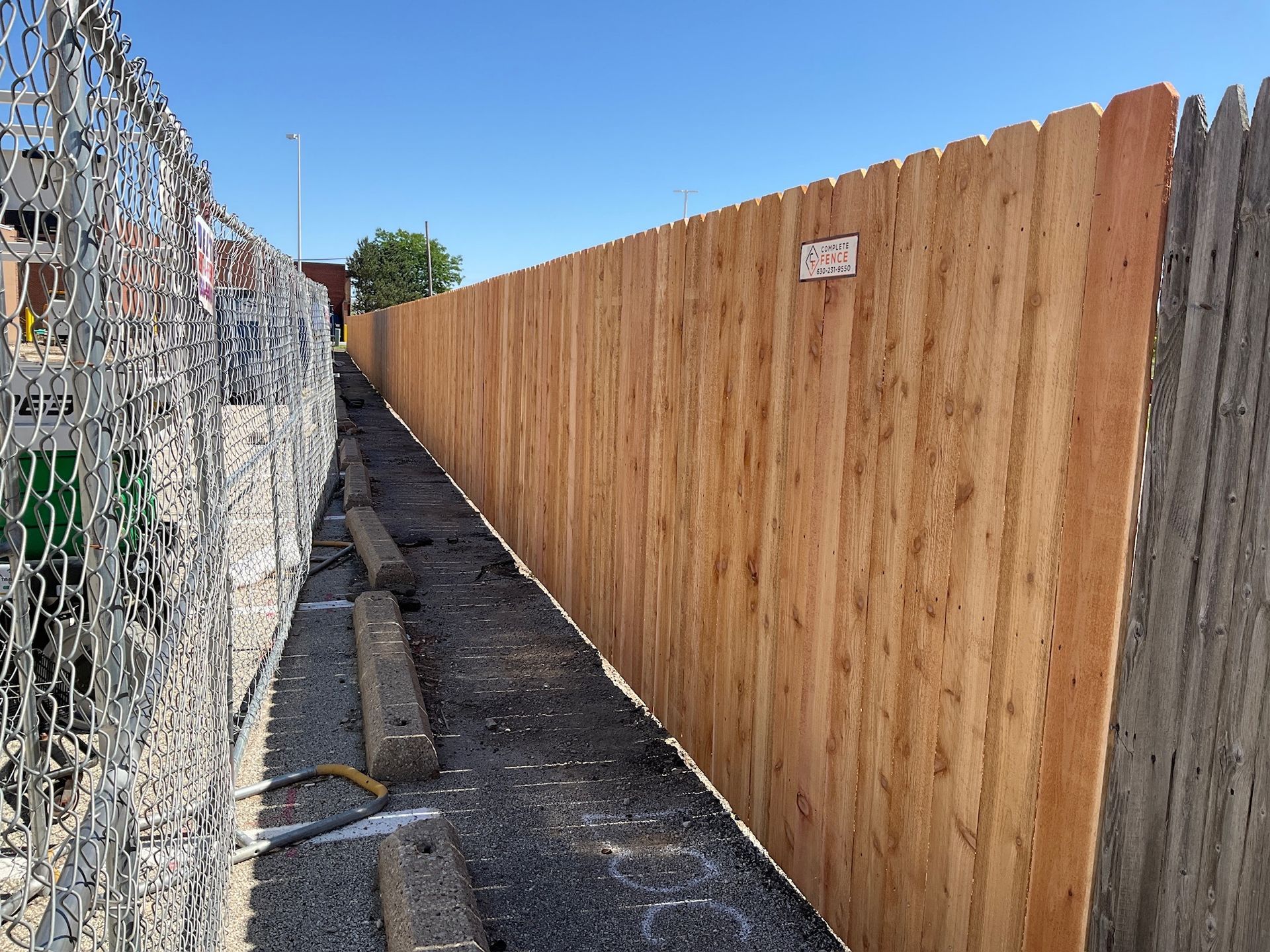 Wooden fence alongside a chain-link fence on a gray surface with a blue sky in the background.