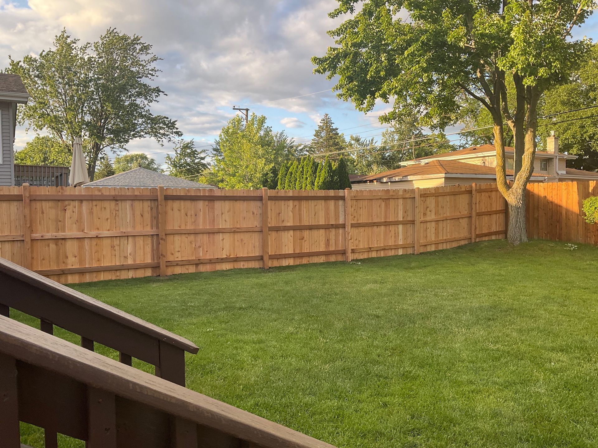 Lawn with wooden fence and trees, view from a deck.