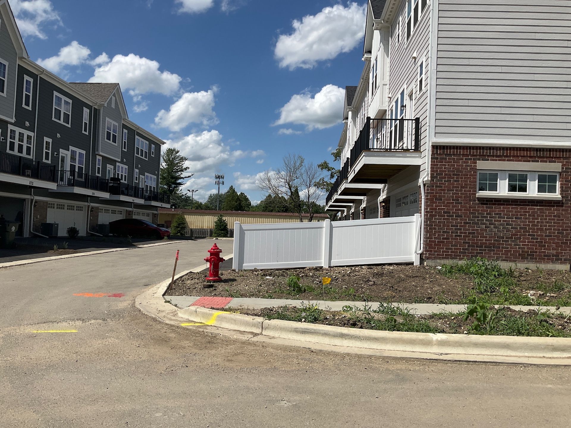 A residential street with townhomes on either side, a fire hydrant, and a white fence under a blue sky.