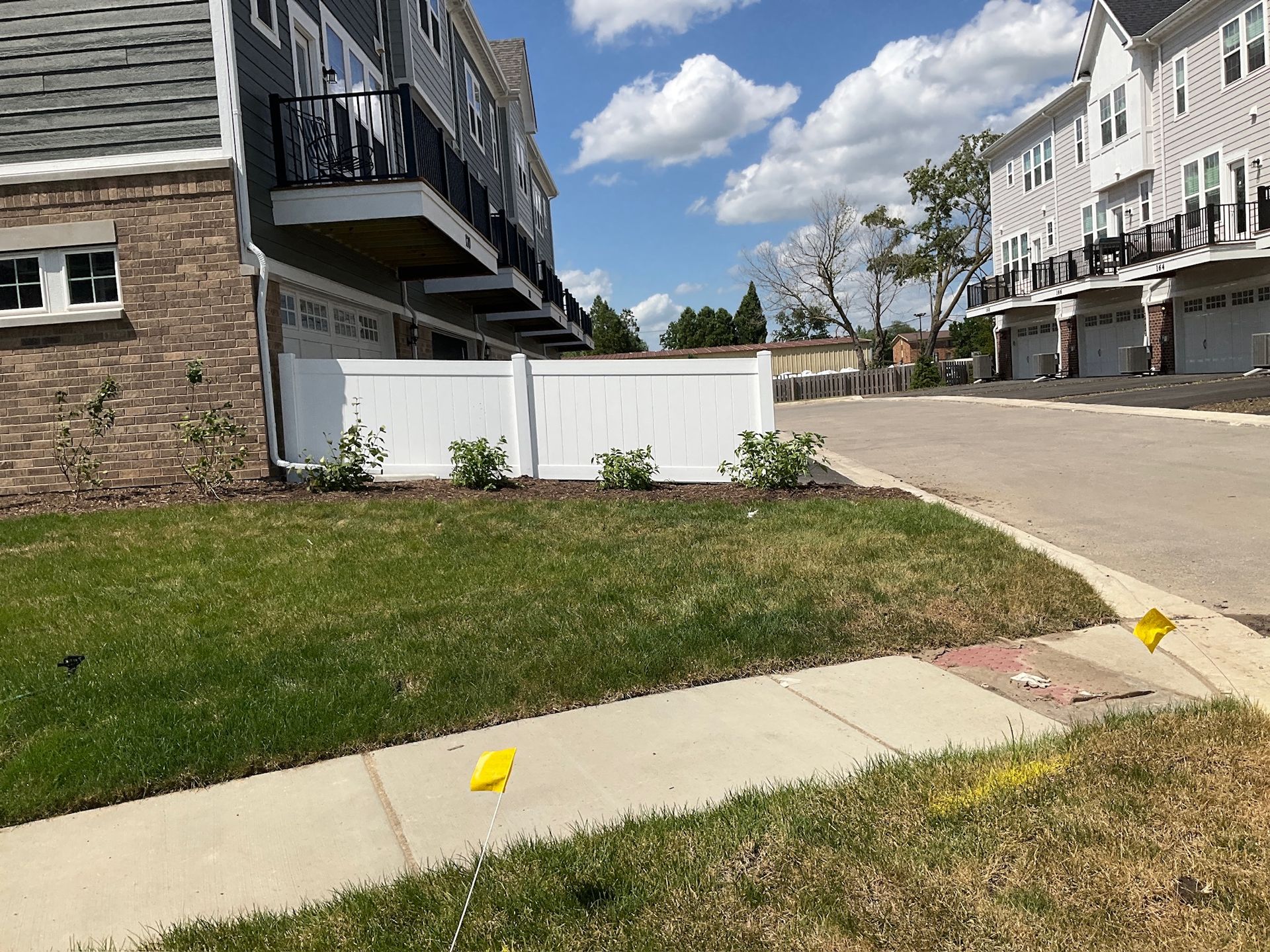 Row of townhouses with a white fence and green lawn on a sunny day.