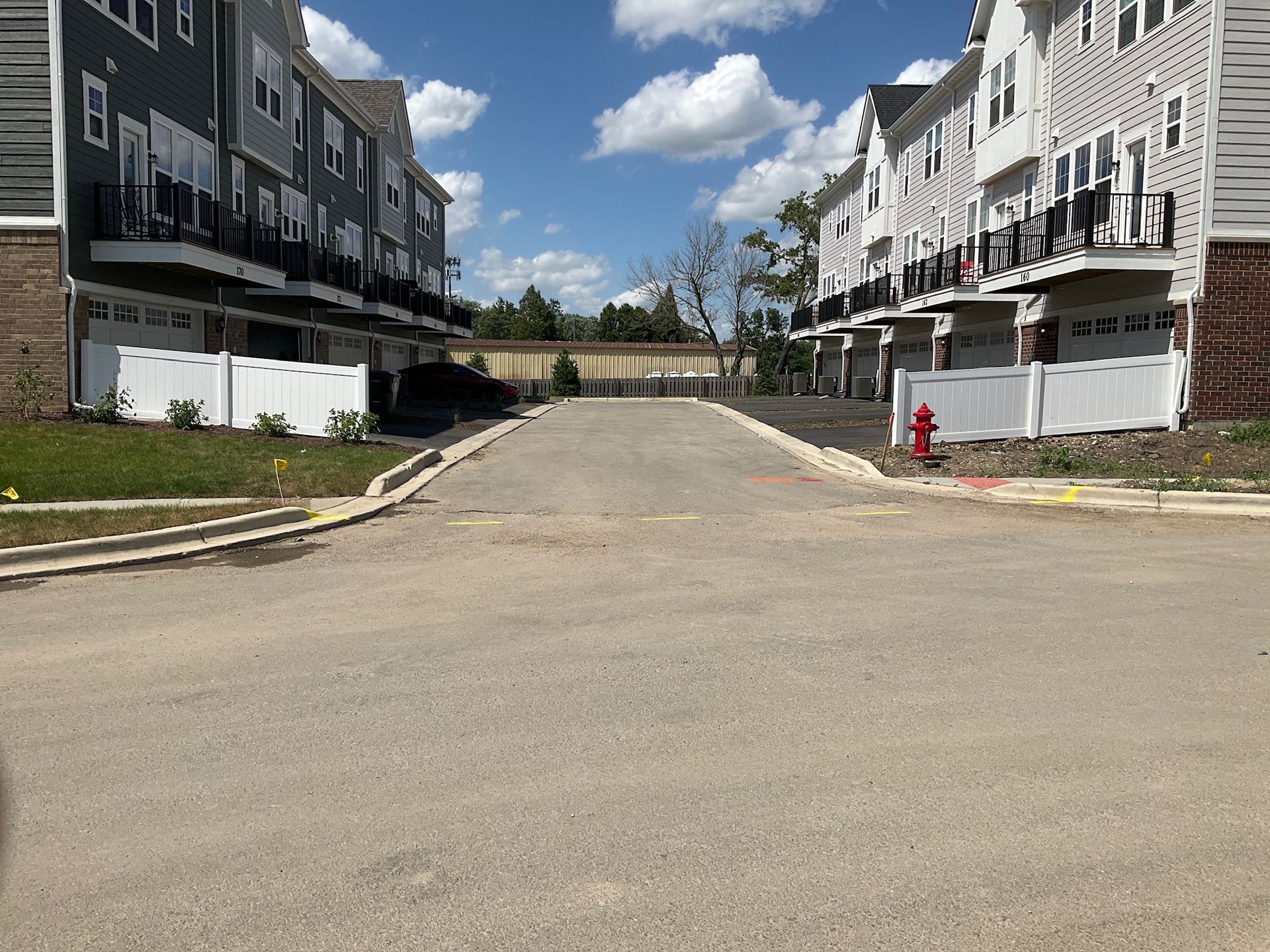 Paved road between townhouses with garages. Blue sky, red fire hydrant.