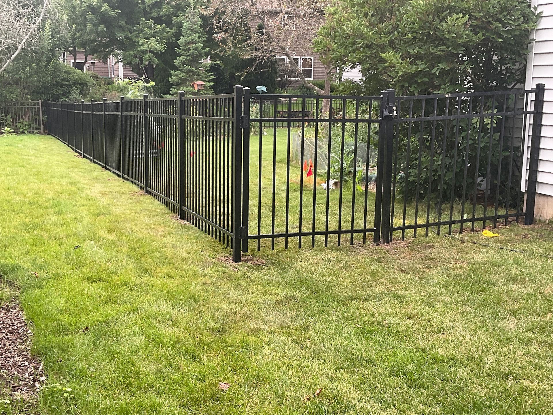 Black metal fence surrounds a grassy yard, beside a house with a white exterior.