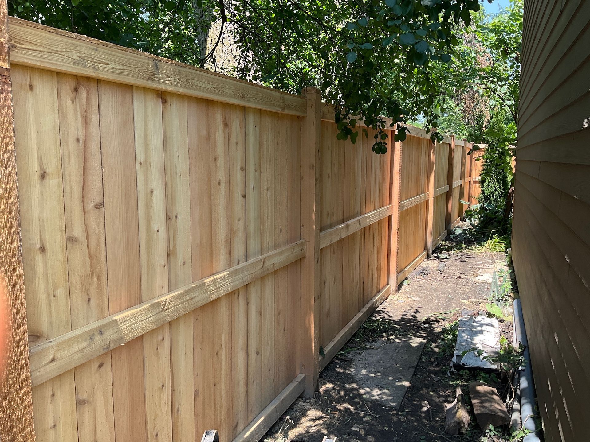 Wooden fence in a residential backyard, with a narrow path and trees alongside it.