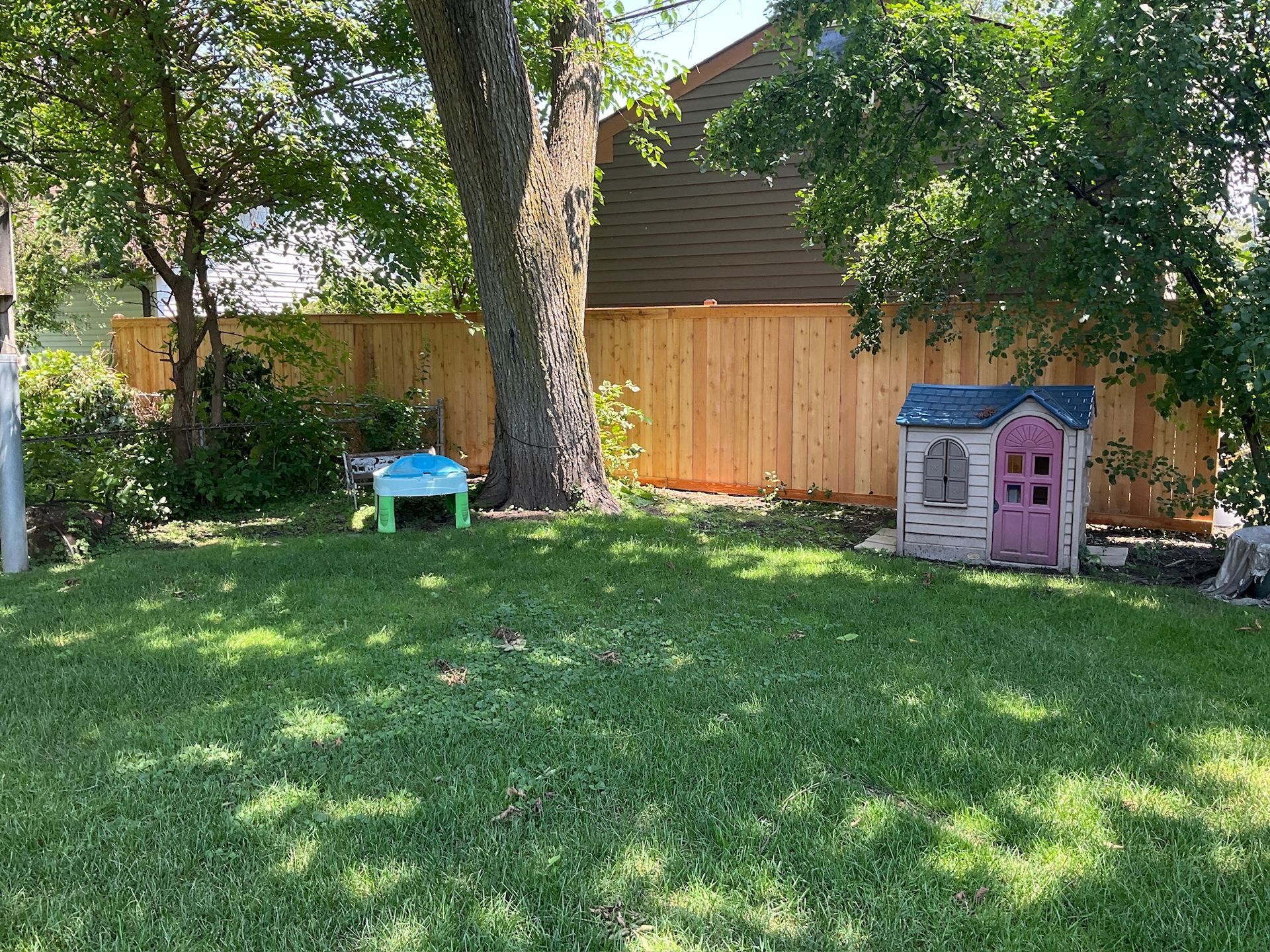 Backyard with a wooden fence, playhouse, table, and tree.