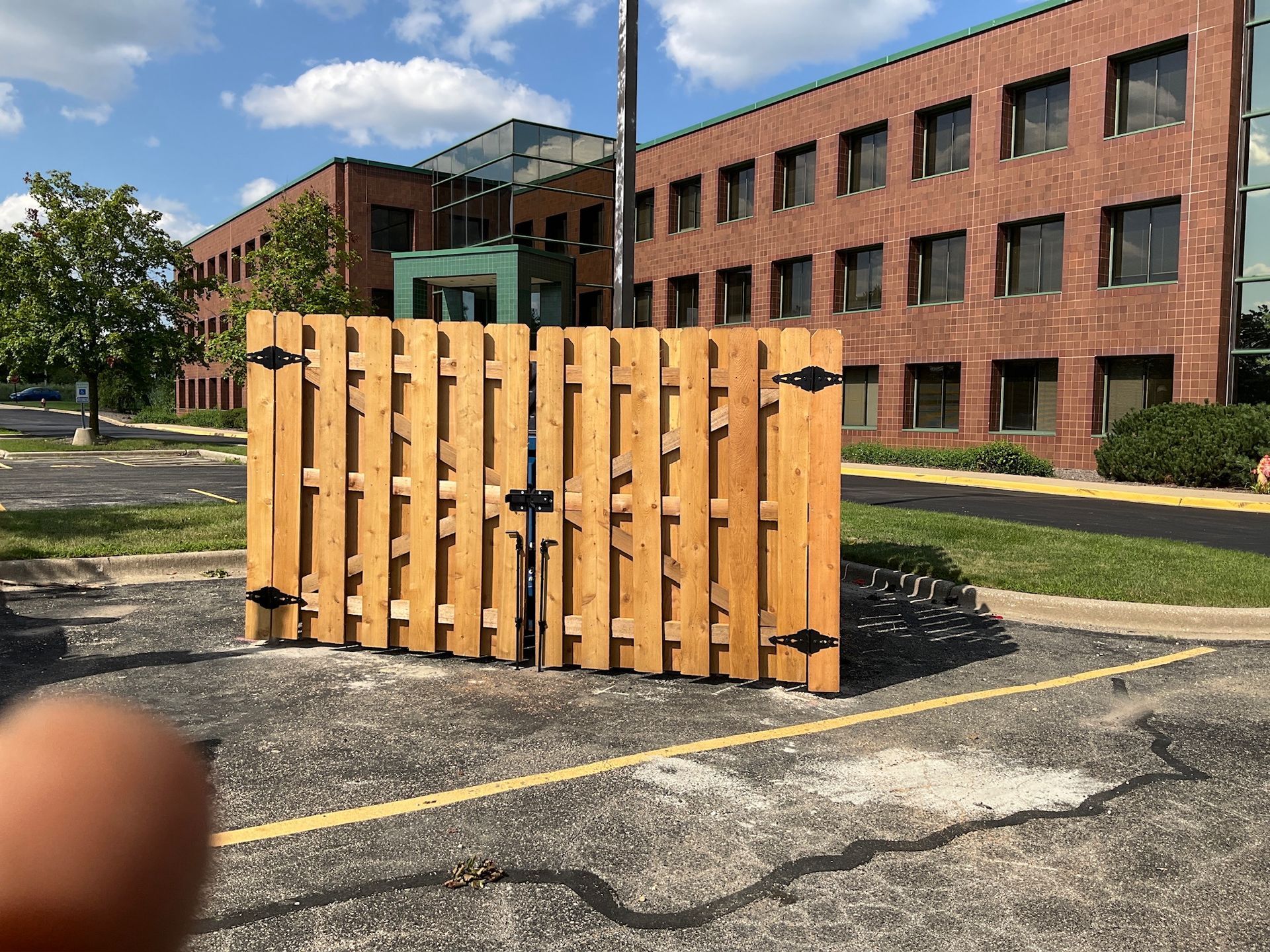 Wooden fence in a parking lot, in front of a brick building.