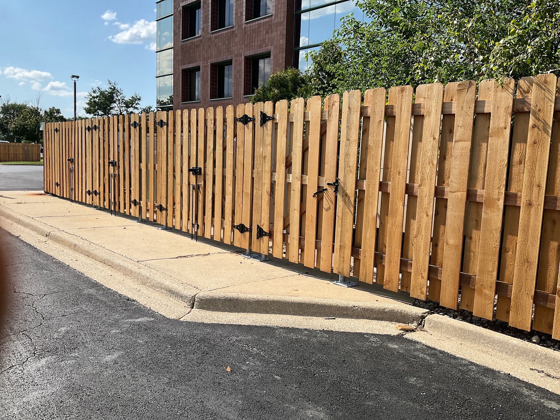 Wooden fence bordering a parking lot with a building and blue sky in the background.