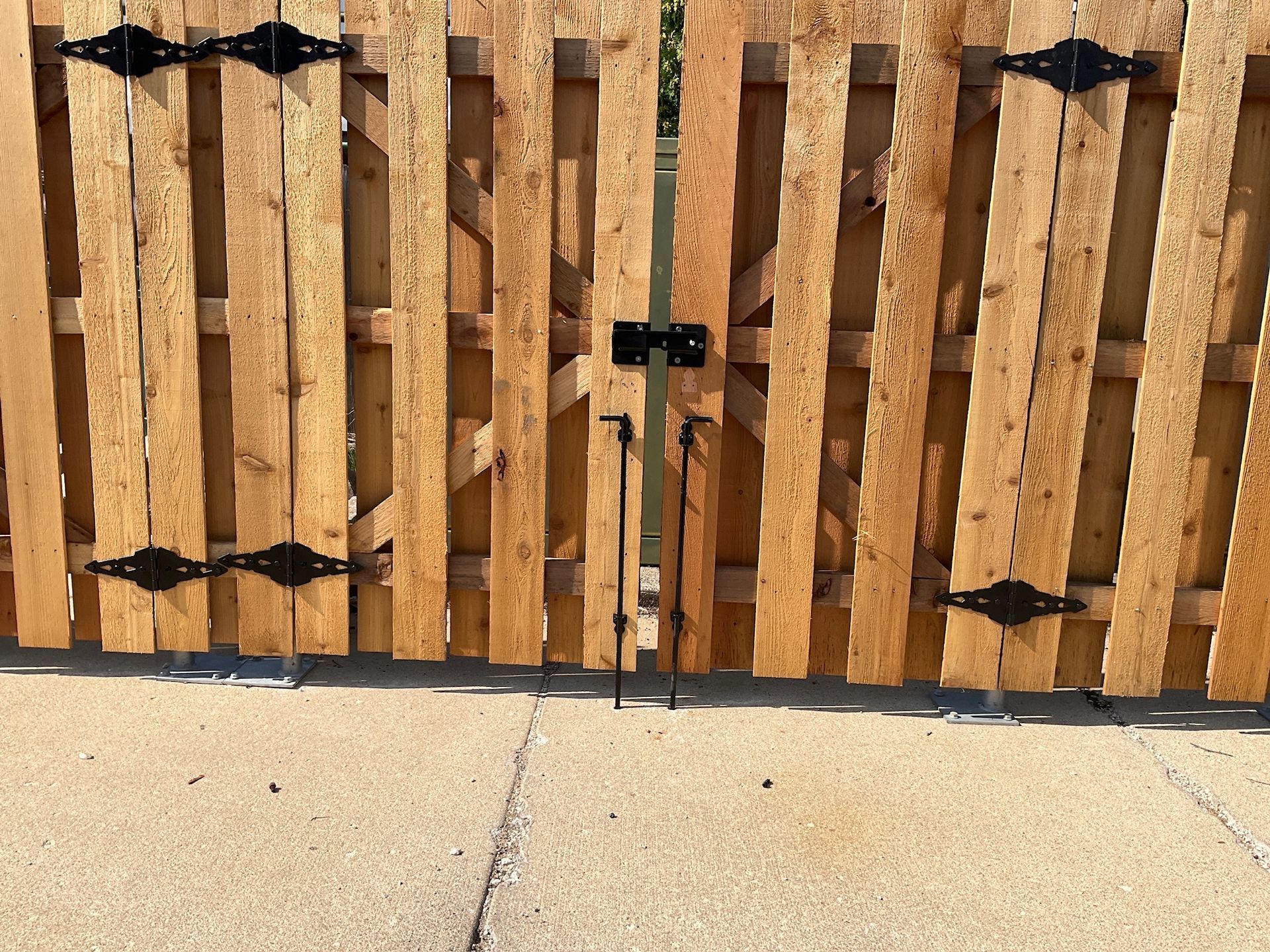 Wooden gate with black hinges and latch, closed on a concrete surface.